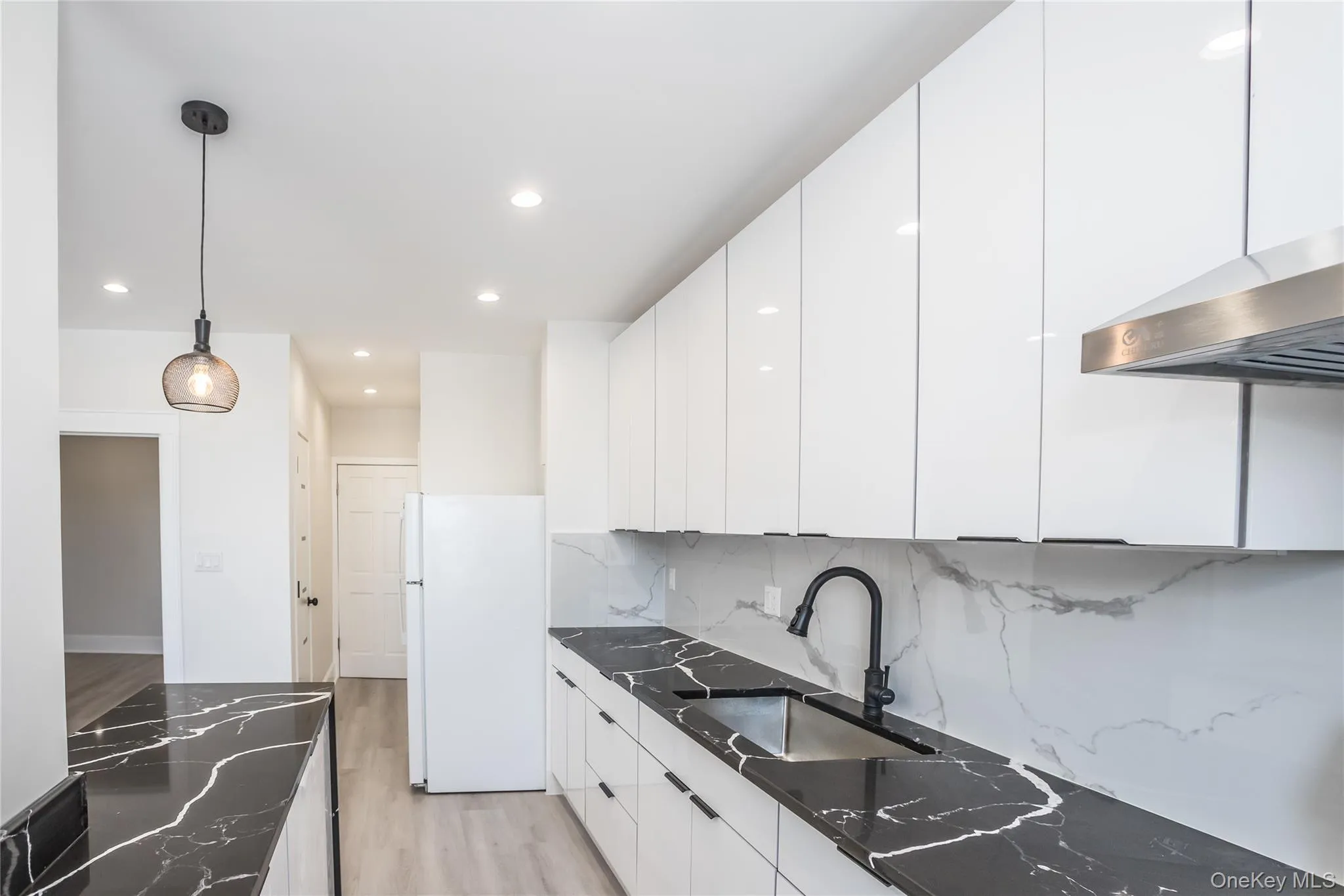 Kitchen featuring freestanding refrigerator, a sink, recessed lighting, light wood-style flooring, and dark stone countertops Kitchen featuring freestanding refrigerator, a sink, recessed lighting, light wood-style flooring, and dark stone countertops