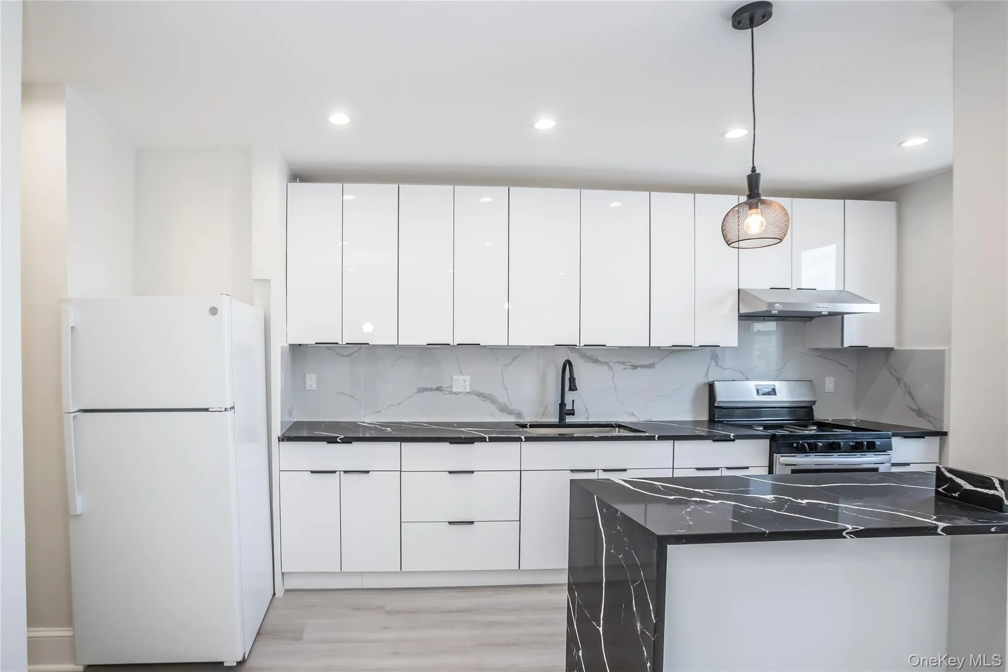 Kitchen featuring freestanding refrigerator, a sink, modern cabinets, stainless steel range with electric stovetop, and under cabinet range hood Kitchen featuring freestanding refrigerator, a sink, modern cabinets, stainless steel range with electric stovetop, and under cabinet range hood