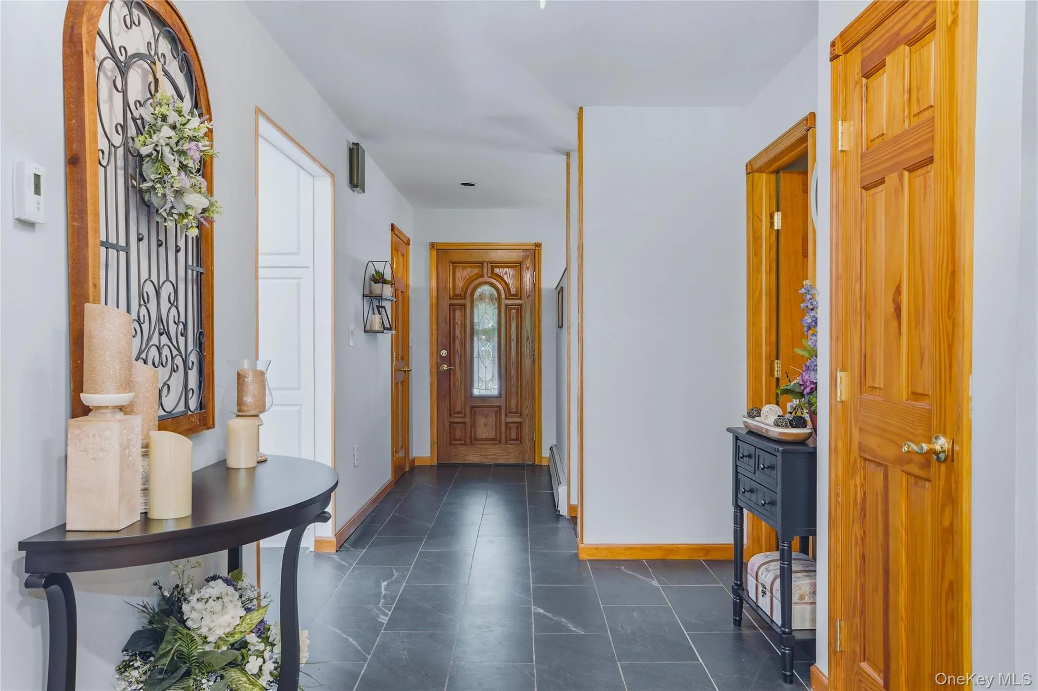 Entryway featuring dark tile flooring, light gray walls, natural wood doors, and a wood-framed arched wall accent Entryway featuring dark tile flooring, light gray walls, natural wood doors, and a wood-framed arched wall accent