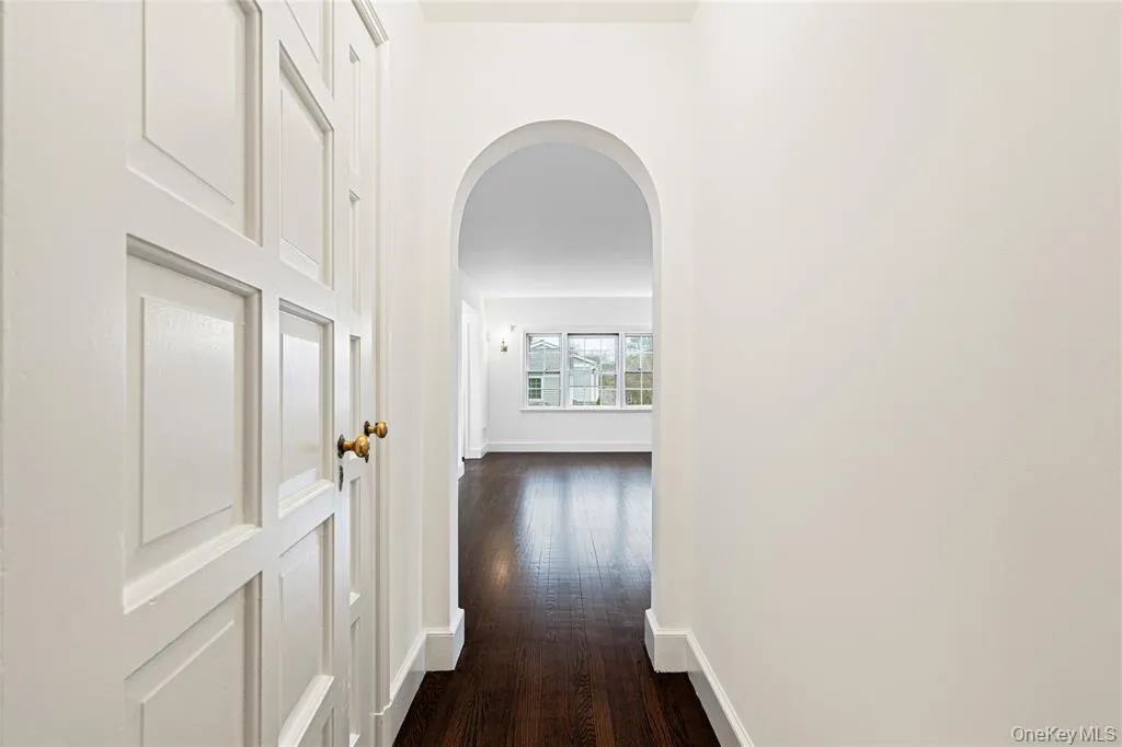 Corridor with arched walkways, dark wood-style flooring, and baseboards Corridor with arched walkways, dark wood-style flooring, and baseboards