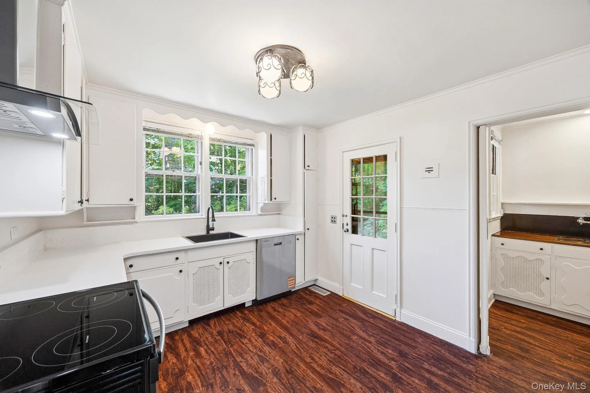 Kitchen featuring wall chimney exhaust hood, dark wood-style flooring, white cabinetry, crown molding, and stainless steel dishwasher Kitchen featuring wall chimney exhaust hood, dark wood-style flooring, white cabinetry, crown molding, and stainless steel dishwasher