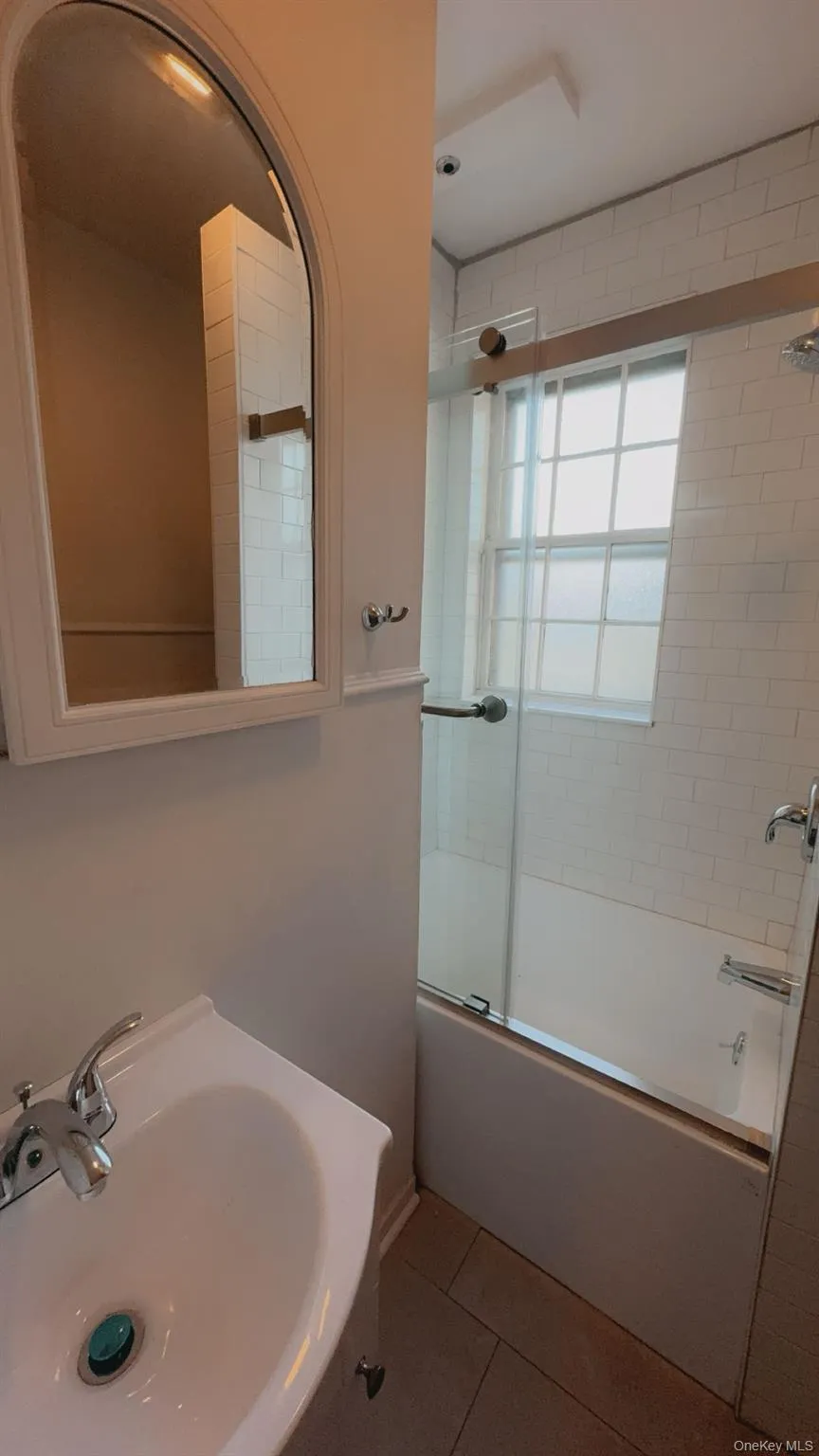 Bathroom with tile patterned flooring, bath / shower combo with glass door, and sink Bathroom with tile patterned flooring, bath / shower combo with glass door, and sink