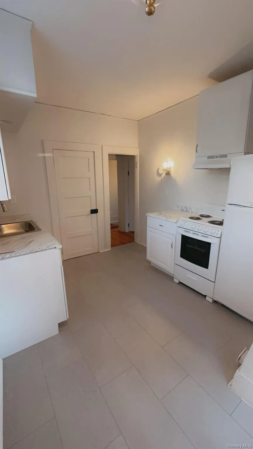 Kitchen featuring white cabinetry, sink, range hood, white appliances, and light tile patterned floors Kitchen featuring white cabinetry, sink, range hood, white appliances, and light tile patterned floors