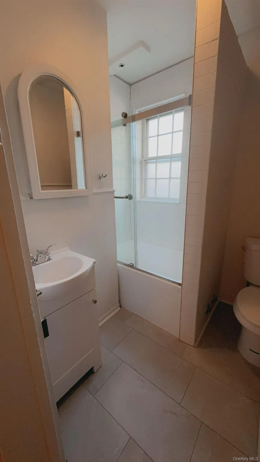 Full bathroom with tile patterned floors, vanity, toilet, and bath / shower combo with glass door Full bathroom with tile patterned floors, vanity, toilet, and bath / shower combo with glass door