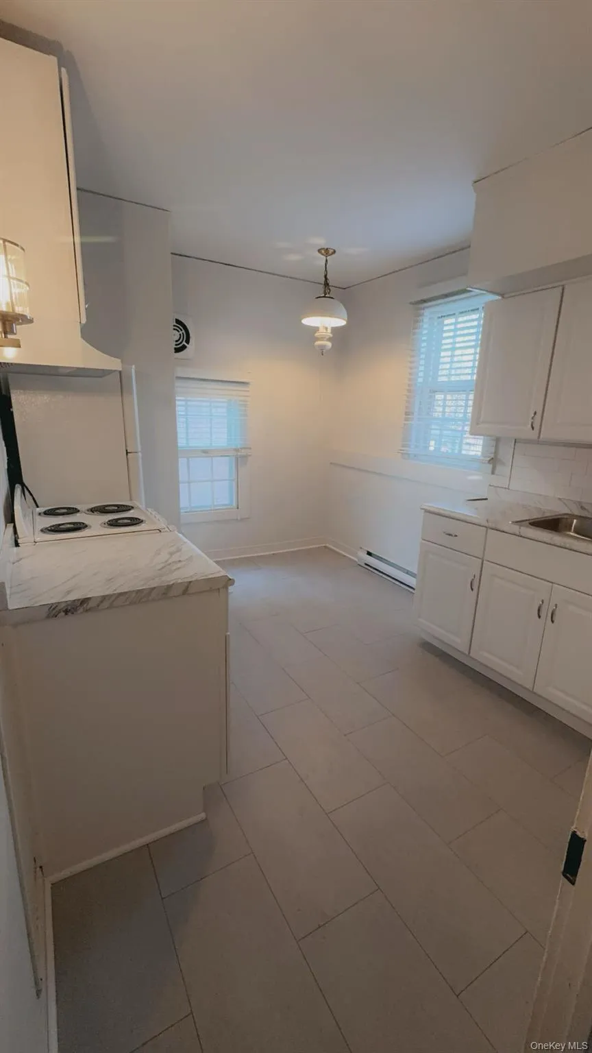 Kitchen featuring white cabinets, sink, hanging light fixtures, baseboard heating, and tasteful backsplash Kitchen featuring white cabinets, sink, hanging light fixtures, baseboard heating, and tasteful backsplash