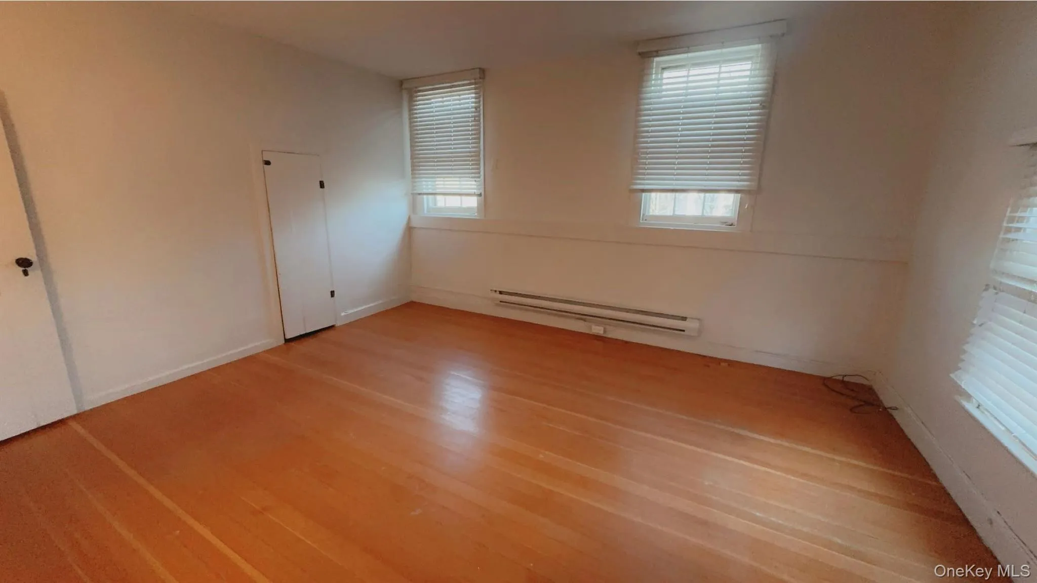 Empty room with a baseboard radiator and hardwood / wood-style flooring Empty room with a baseboard radiator and hardwood / wood-style flooring