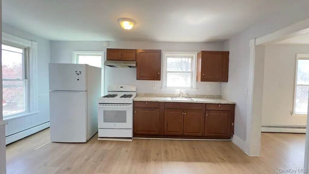 Eat in kitchen with a baseboard radiator, under cabinet range hood, white appliances, and light wood-style floors Eat in kitchen with a baseboard radiator, under cabinet range hood, white appliances, and light wood-style floors
