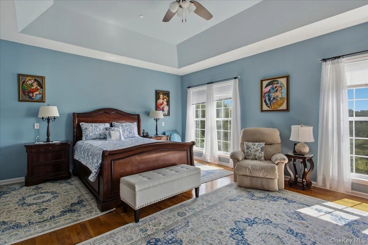 Spacious bedroom featuring light blue walls, hardwood flooring, a tray ceiling, and a ceiling fan Spacious bedroom featuring light blue walls, hardwood flooring, a tray ceiling, and a ceiling fan