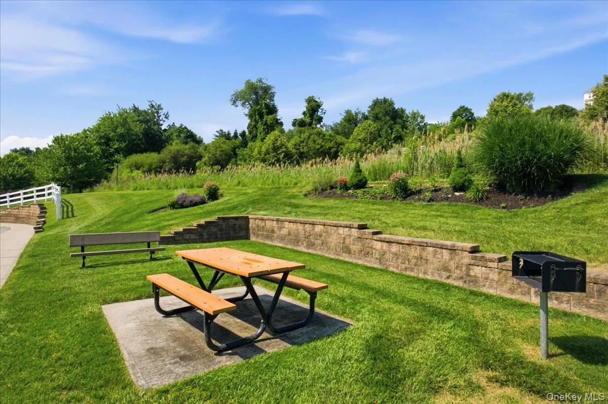 Expansive outdoor area featuring a picnic table on a concrete pad, a built-in barbecue grill, and tiered landscaping Expansive outdoor area featuring a picnic table on a concrete pad, a built-in barbecue grill, and tiered landscaping