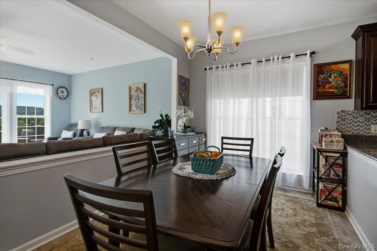 Dining area featuring a dark wood-finish table with coordinating chairs, a contemporary chandelier, and a large window with sheer white curtains Dining area featuring a dark wood-finish table with coordinating chairs, a contemporary chandelier, and a large window with sheer white curtains