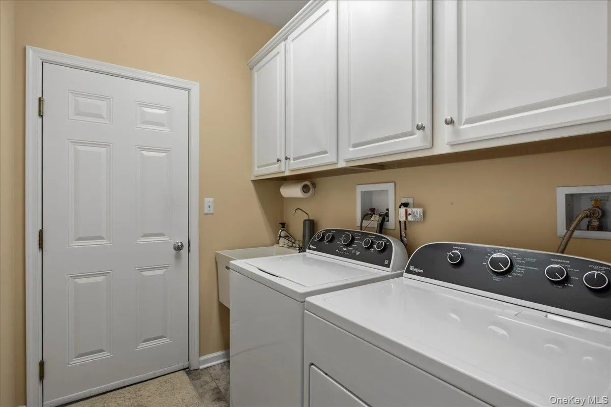 Laundry area featuring white cabinetry, a utility sink, and durable tile flooring Laundry area featuring white cabinetry, a utility sink, and durable tile flooring