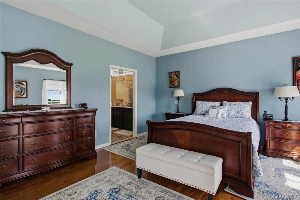 Spacious bedroom featuring wood-finish flooring and a tray ceiling Spacious bedroom featuring wood-finish flooring and a tray ceiling