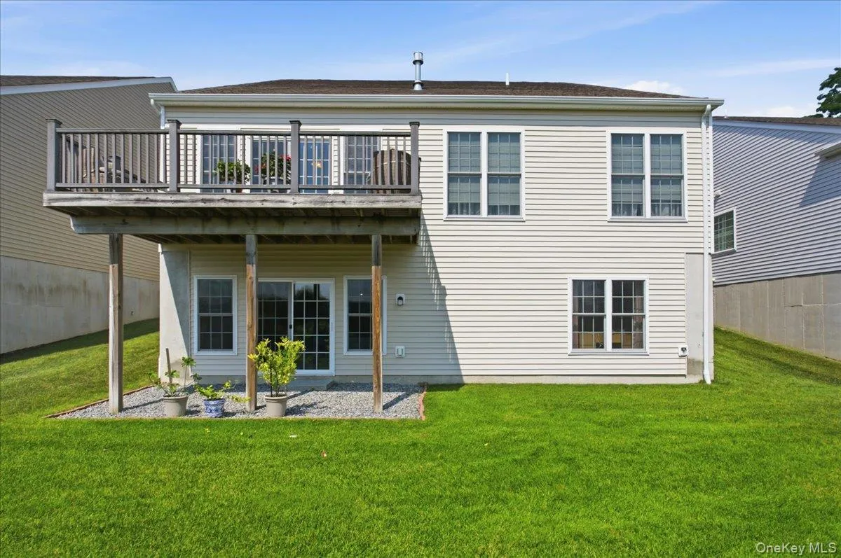 Rear exterior featuring a spacious elevated deck, lower-level sliding glass door access to the yard, multiple windows, light-colored siding, and a sloped grassy lawn Rear exterior featuring a spacious elevated deck, lower-level sliding glass door access to the yard, multiple windows, light-colored siding, and a sloped grassy lawn