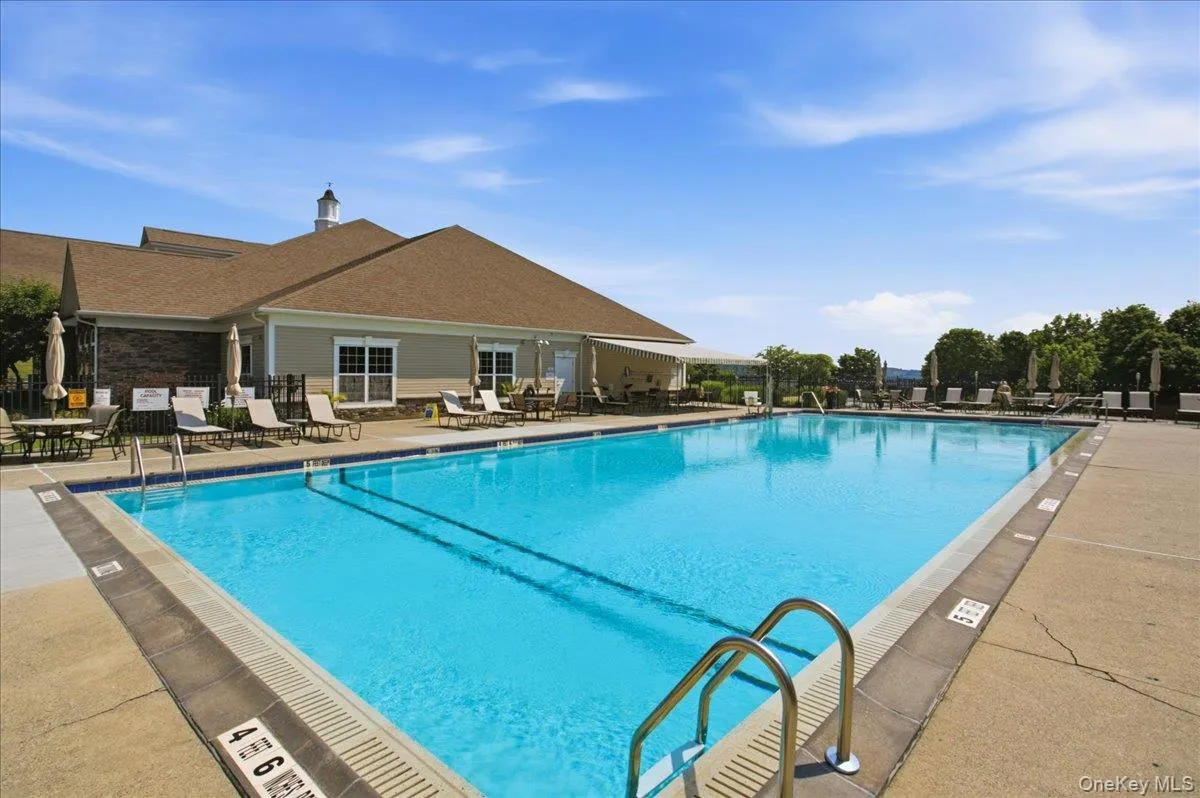 Expansive outdoor swimming pool with a concrete surround, adjacent to a clubhouse building featuring a cupola Expansive outdoor swimming pool with a concrete surround, adjacent to a clubhouse building featuring a cupola