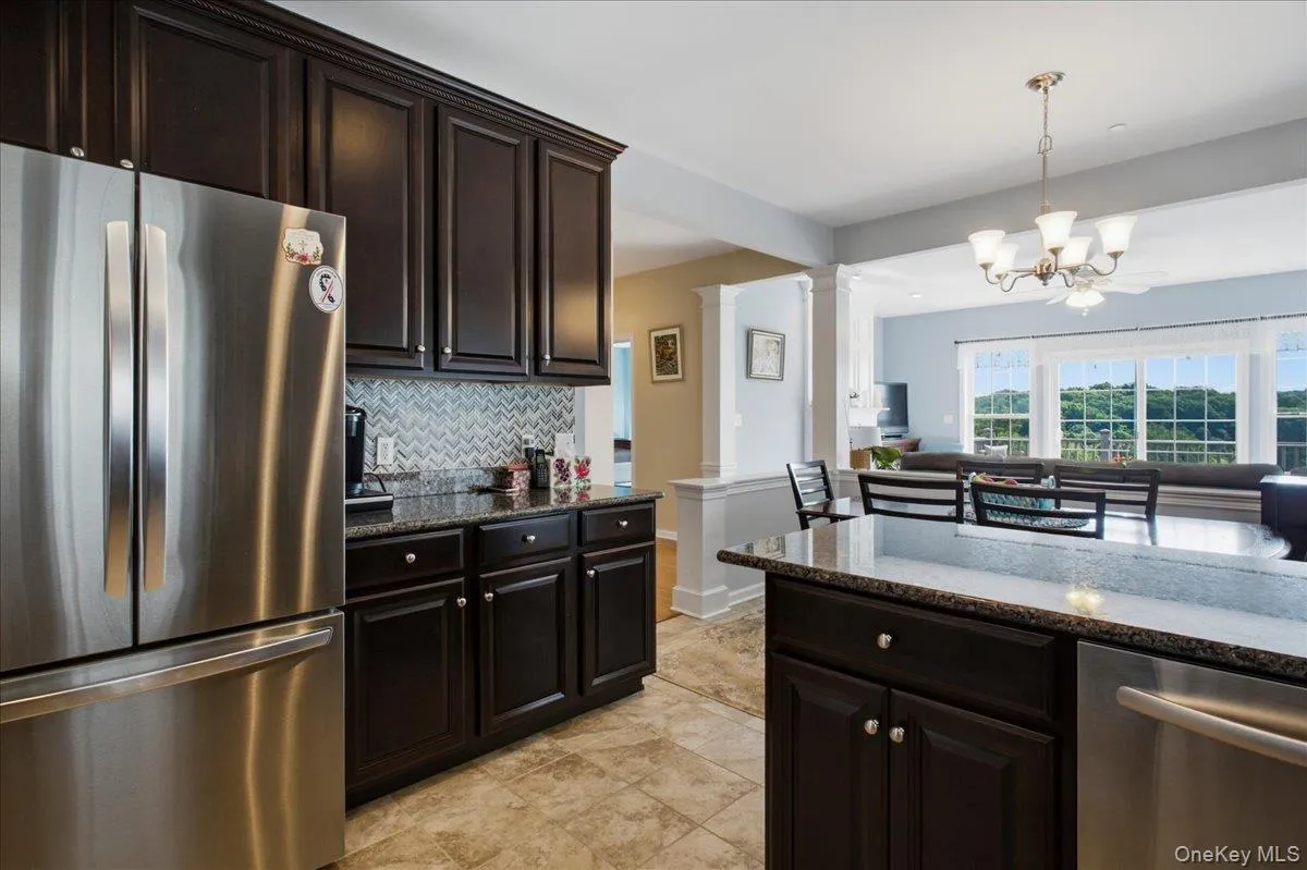 Kitchen featuring dark wood cabinetry, stainless steel appliances, a tile backsplash with a chevron pattern, and granite countertops Kitchen featuring dark wood cabinetry, stainless steel appliances, a tile backsplash with a chevron pattern, and granite countertops