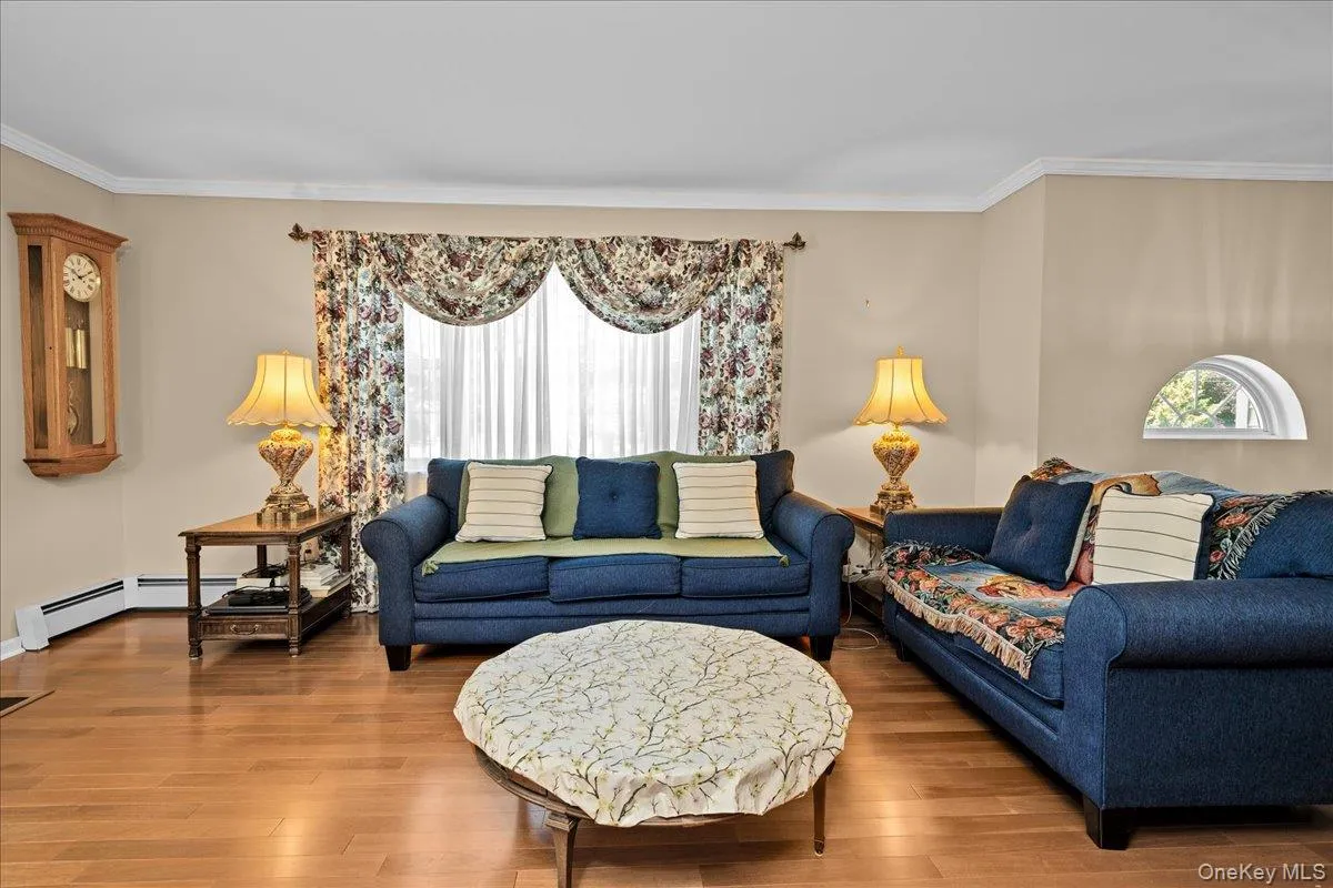 Living room area featuring wood-finish flooring, a large window with valance, crown molding, and a built-in arched window Living room area featuring wood-finish flooring, a large window with valance, crown molding, and a built-in arched window