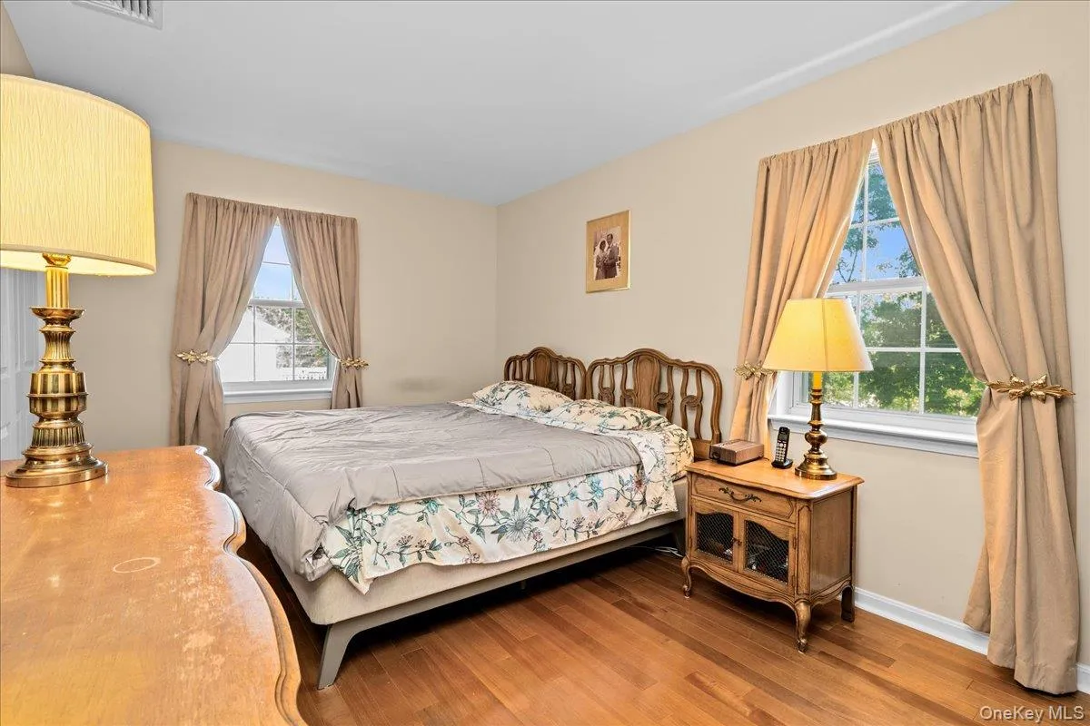 Bedroom 1 featuring two large windows, light cream wall paint, and wood-finish flooring Bedroom 1 featuring two large windows, light cream wall paint, and wood-finish flooring