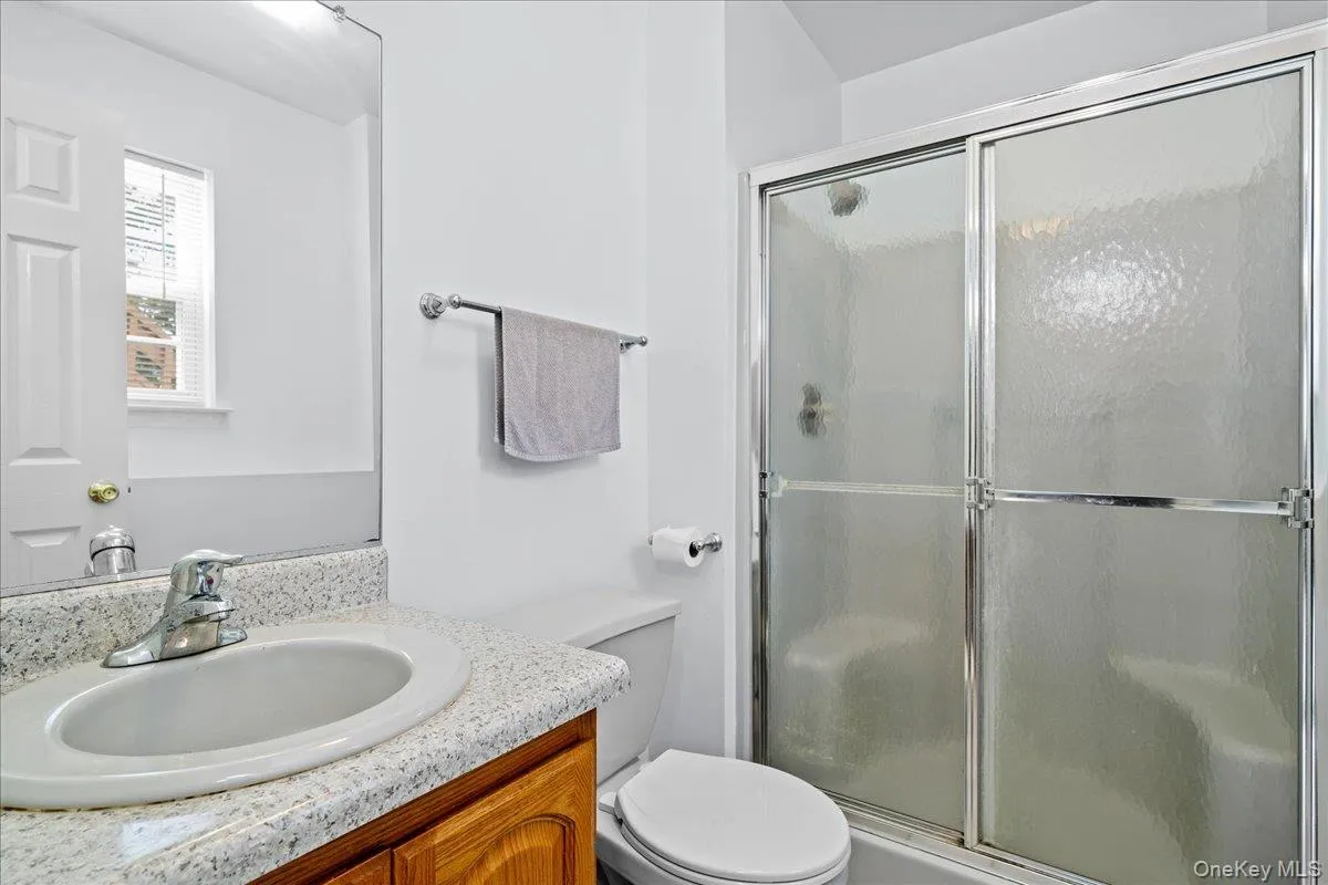 Full bath featuring a shower with sliding textured glass doors, a vanity with a white oval sink, a speckled countertop, and wood-finish cabinetry Full bath featuring a shower with sliding textured glass doors, a vanity with a white oval sink, a speckled countertop, and wood-finish cabinetry