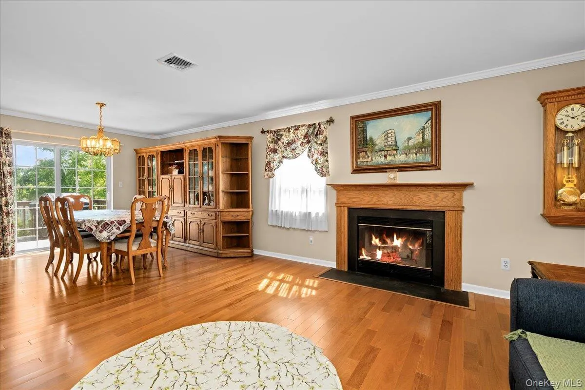Hardwood flooring throughout featuring a wood burning fireplace with a wood mantle and black hearth, crown molding, and sliding glass doors Hardwood flooring throughout featuring a wood burning fireplace with a wood mantle and black hearth, crown molding, and sliding glass doors