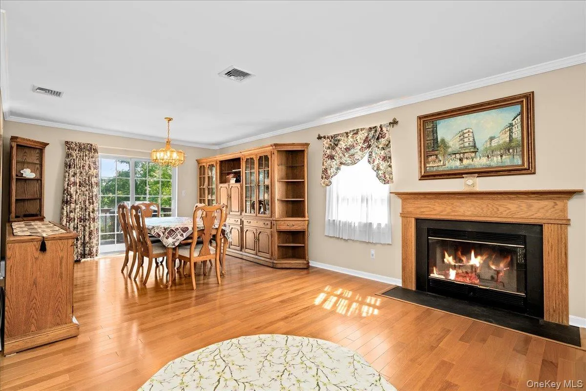 Hardwood flooring throughout featuring a wood burning fireplace with a wood mantle and black hearth, crown molding, and sliding glass doors Hardwood flooring throughout featuring a wood burning fireplace with a wood mantle and black hearth, crown molding, and sliding glass doors