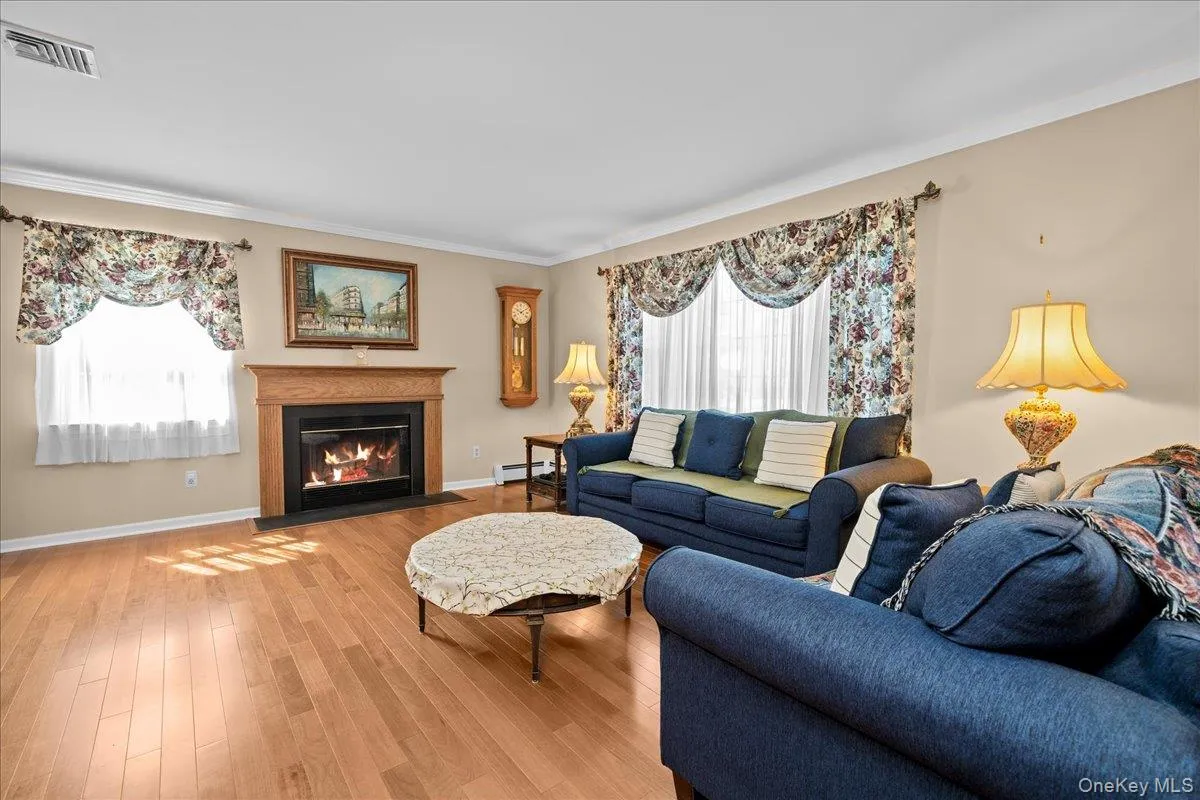 Living room featuring wood-finish flooring, a wood-buning fireplace with a wood mantle, and crown molding Living room featuring wood-finish flooring, a wood-buning fireplace with a wood mantle, and crown molding