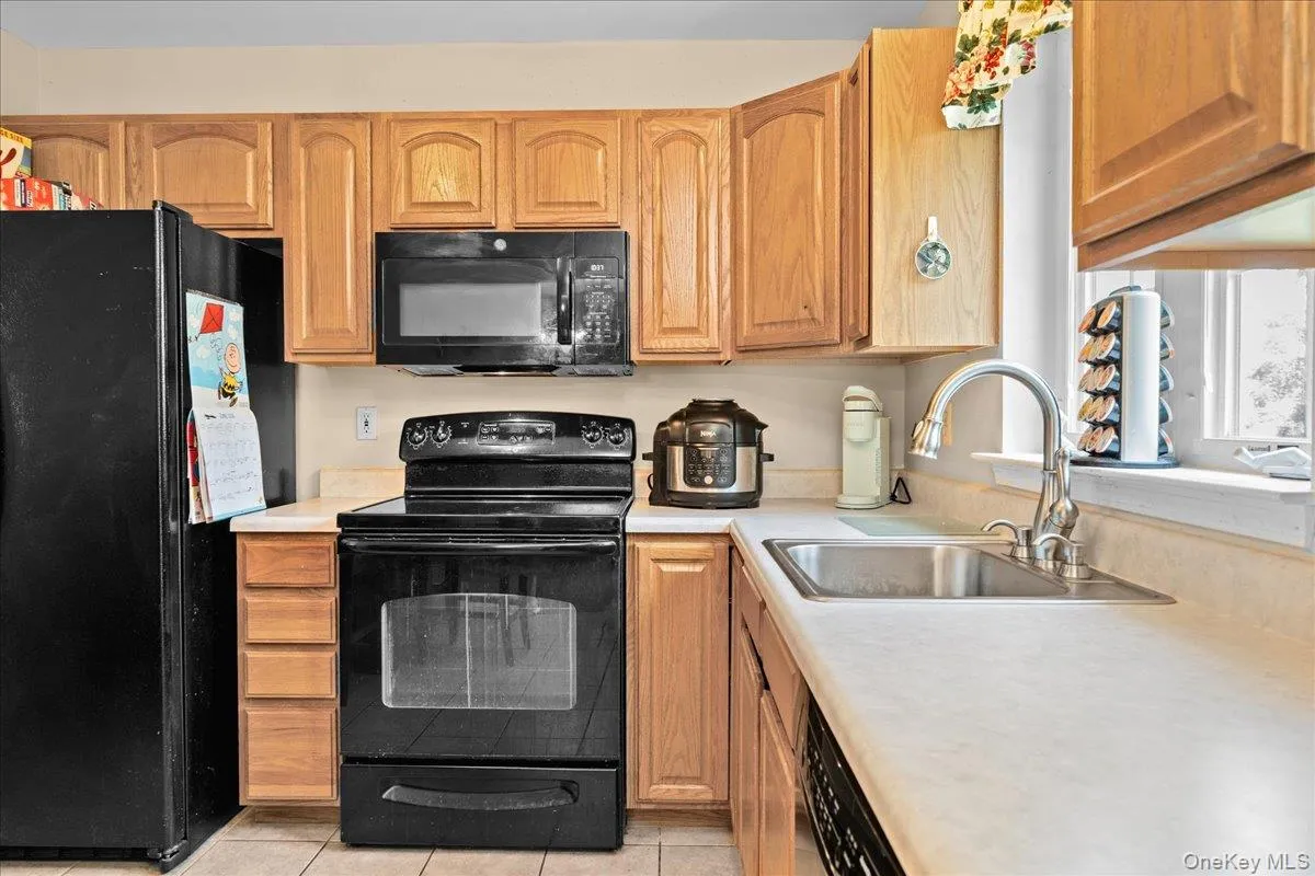 Kitchen featuring nice wood cabinetry, light-toned countertops, tile flooring, and a stainless steel sink with a gooseneck faucet Kitchen featuring nice wood cabinetry, light-toned countertops, tile flooring, and a stainless steel sink with a gooseneck faucet