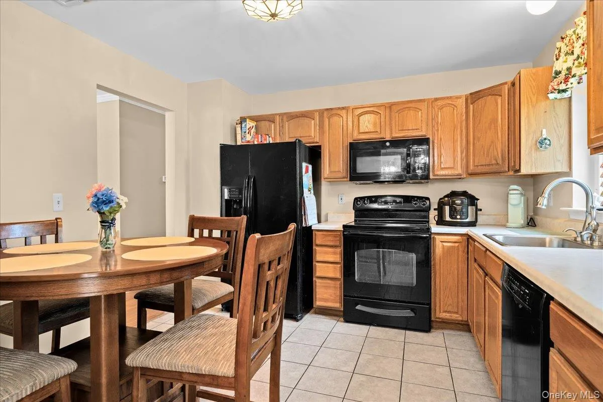 Kitchen featuring nice wood-finish cabinetry, black appliances including a refrigerator and range, a stainless steel sink, and light-toned countertops Kitchen featuring nice wood-finish cabinetry, black appliances including a refrigerator and range, a stainless steel sink, and light-toned countertops