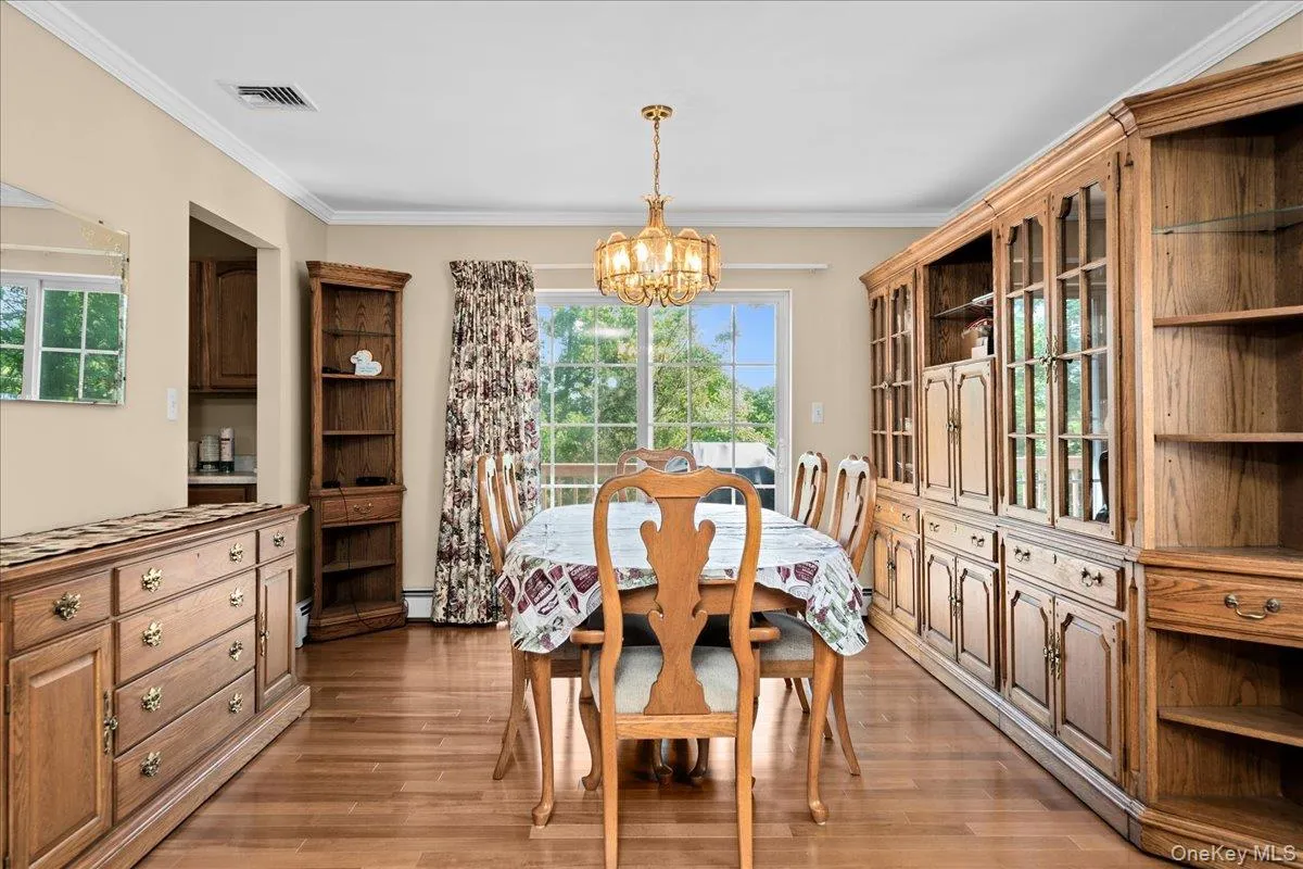 Dining room area featuring wood-finish flooring, a glass-paned sliding door, a brass chandelier, and crown molding Dining room area featuring wood-finish flooring, a glass-paned sliding door, a brass chandelier, and crown molding