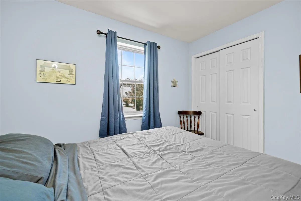 Bedroom 2 featuring a window with a rod and drapes, light blue wall paint, and a two-door closet with panel detailing Bedroom 2 featuring a window with a rod and drapes, light blue wall paint, and a two-door closet with panel detailing