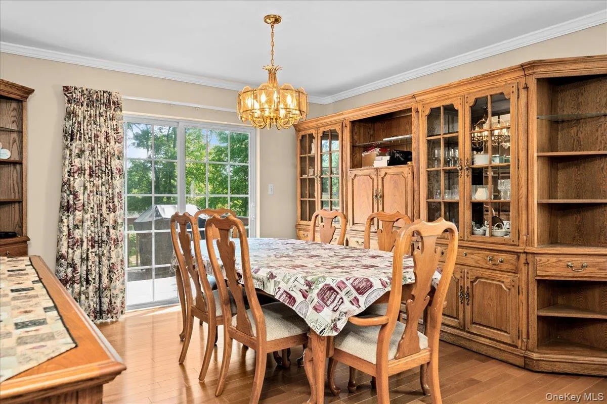 Dining room area featuring wood-finish flooring, a brass chandelier, crown molding, and a built-in wood cabinetry unit with glass-front doors Dining room area featuring wood-finish flooring, a brass chandelier, crown molding, and a built-in wood cabinetry unit with glass-front doors