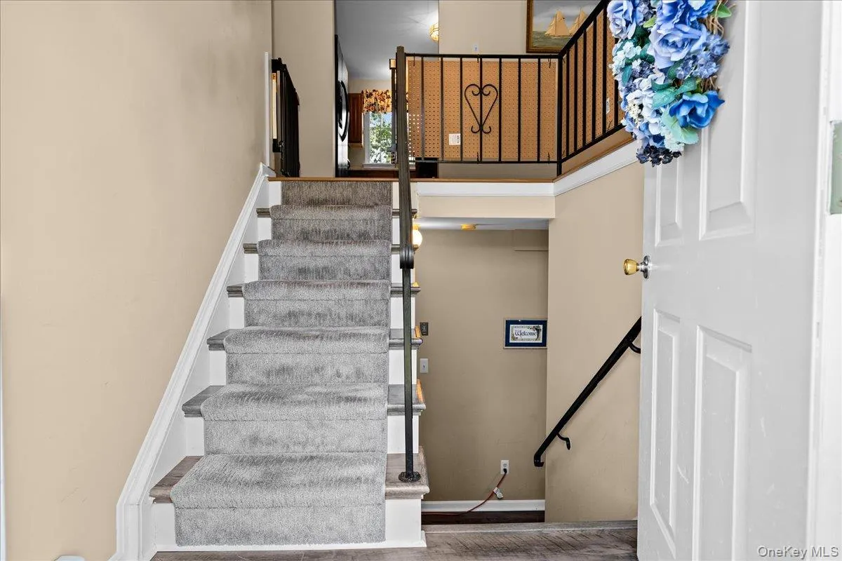 Entry featuring a carpeted staircase with white risers and a black metal railing Entry featuring a carpeted staircase with white risers and a black metal railing