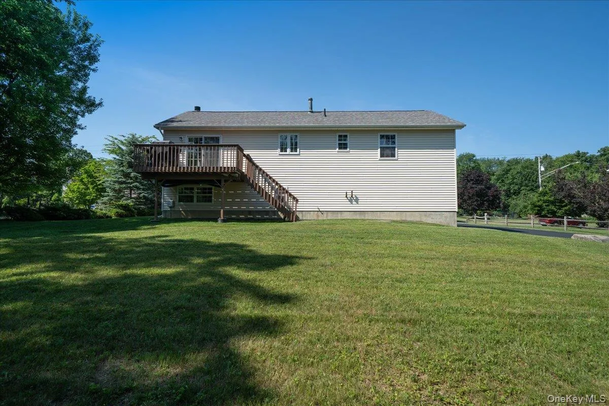Big backyard featuring a manicured lawn, a wooden deck with railing, and stairs Big backyard featuring a manicured lawn, a wooden deck with railing, and stairs