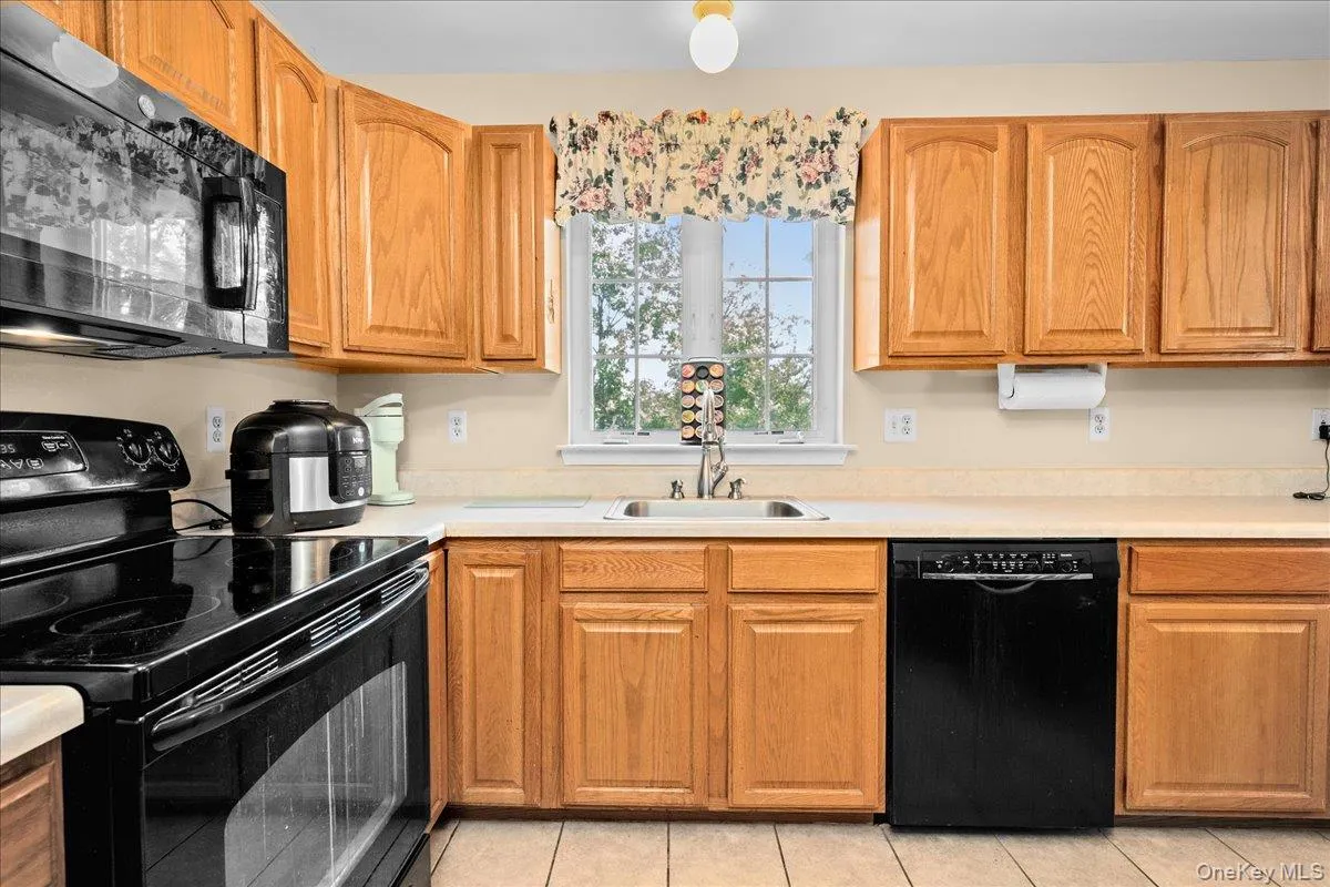 Kitchen featuring nice wood-finish cabinetry, black appliances, light-toned countertops, and tile flooring Kitchen featuring nice wood-finish cabinetry, black appliances, light-toned countertops, and tile flooring