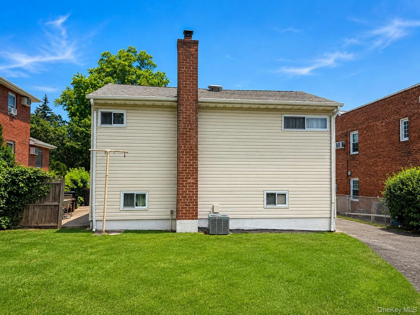 Expansive lawn bordering the property, featuring a brick chimney, light-colored siding, and a visible HVAC unit Expansive lawn bordering the property, featuring a brick chimney, light-colored siding, and a visible HVAC unit