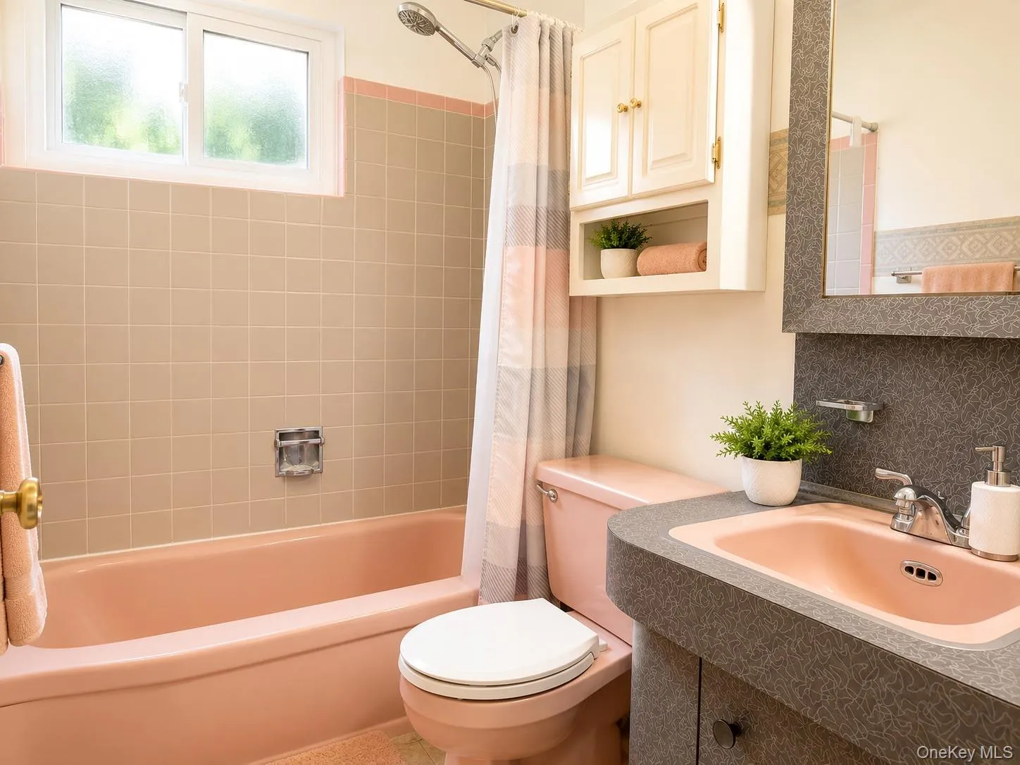 Bathroom featuring a pink tub and toilet, a matching pink sink, and dark patterned countertop Bathroom featuring a pink tub and toilet, a matching pink sink, and dark patterned countertop