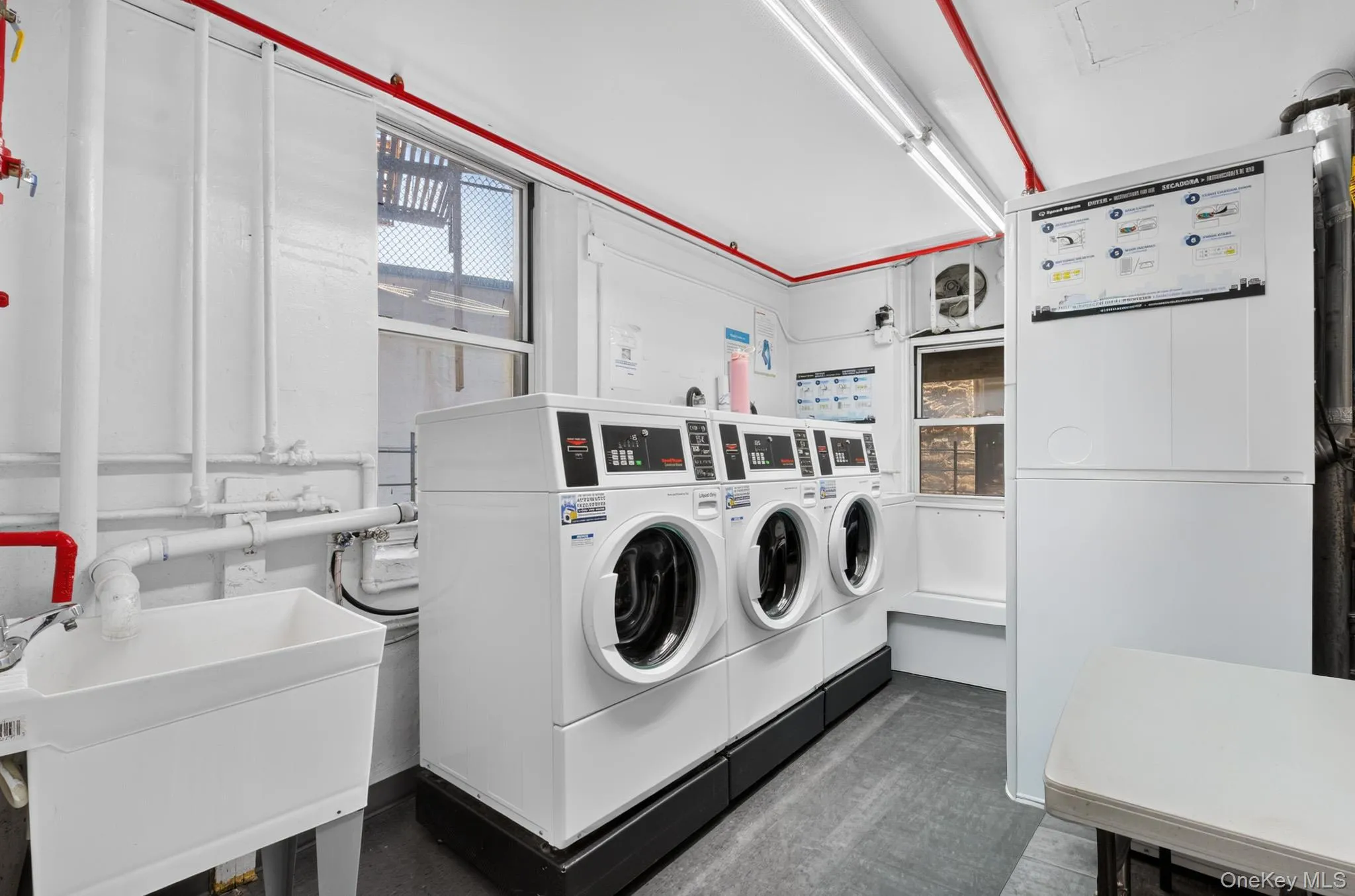 On-site laundry facility featuring multiple front-loading washers, a utility sink, and ample overhead lighting On-site laundry facility featuring multiple front-loading washers, a utility sink, and ample overhead lighting