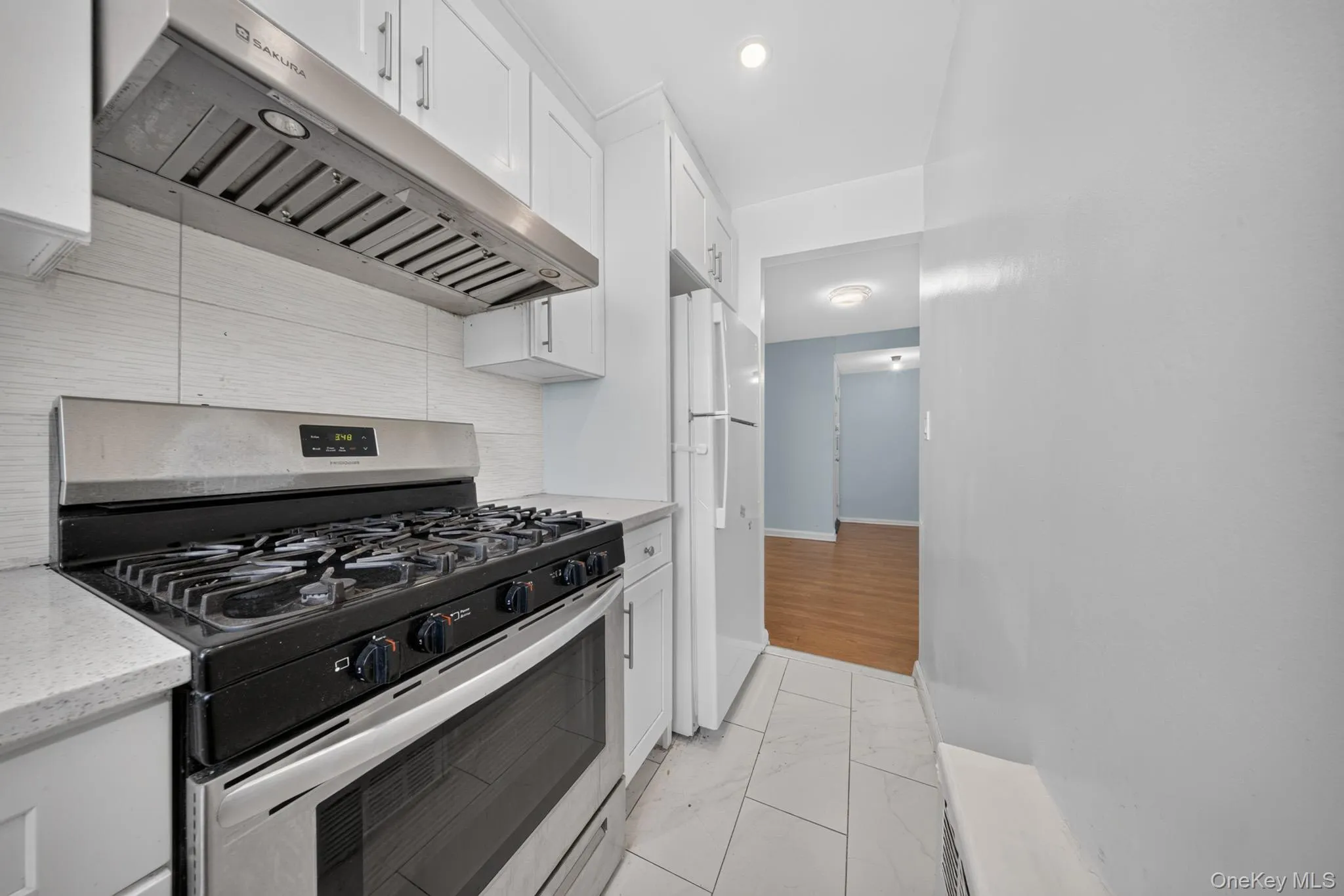 Modern kitchen featuring stainless steel range, coordinating range hood, white shaker-style cabinetry, light countertops, and tile flooring Modern kitchen featuring stainless steel range, coordinating range hood, white shaker-style cabinetry, light countertops, and tile flooring