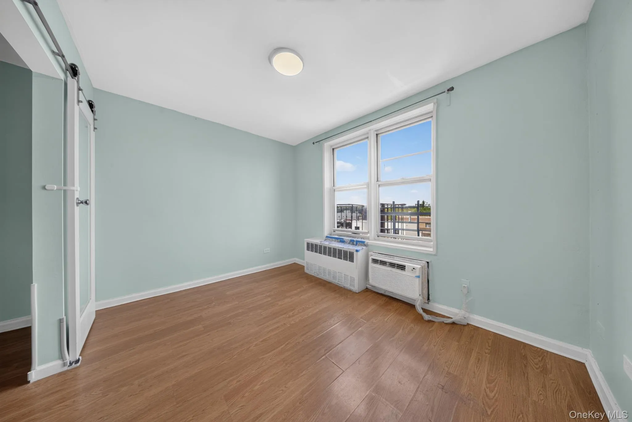 Interior room featuring wood-finish flooring, a large window, and a ceiling-mounted light fixture Interior room featuring wood-finish flooring, a large window, and a ceiling-mounted light fixture