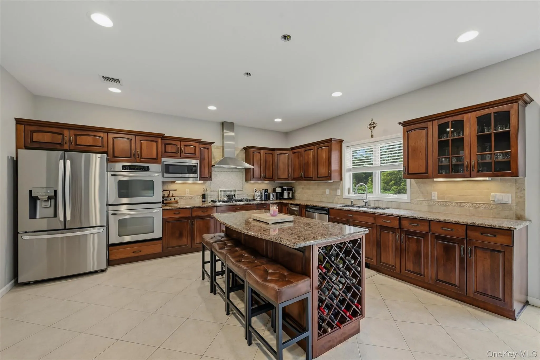 Kitchen featuring extensive wood cabinetry, stainless steel appliances, a center island with integrated wine storage, granite countertops, and tile flooring Kitchen featuring extensive wood cabinetry, stainless steel appliances, a center island with integrated wine storage, granite countertops, and tile flooring