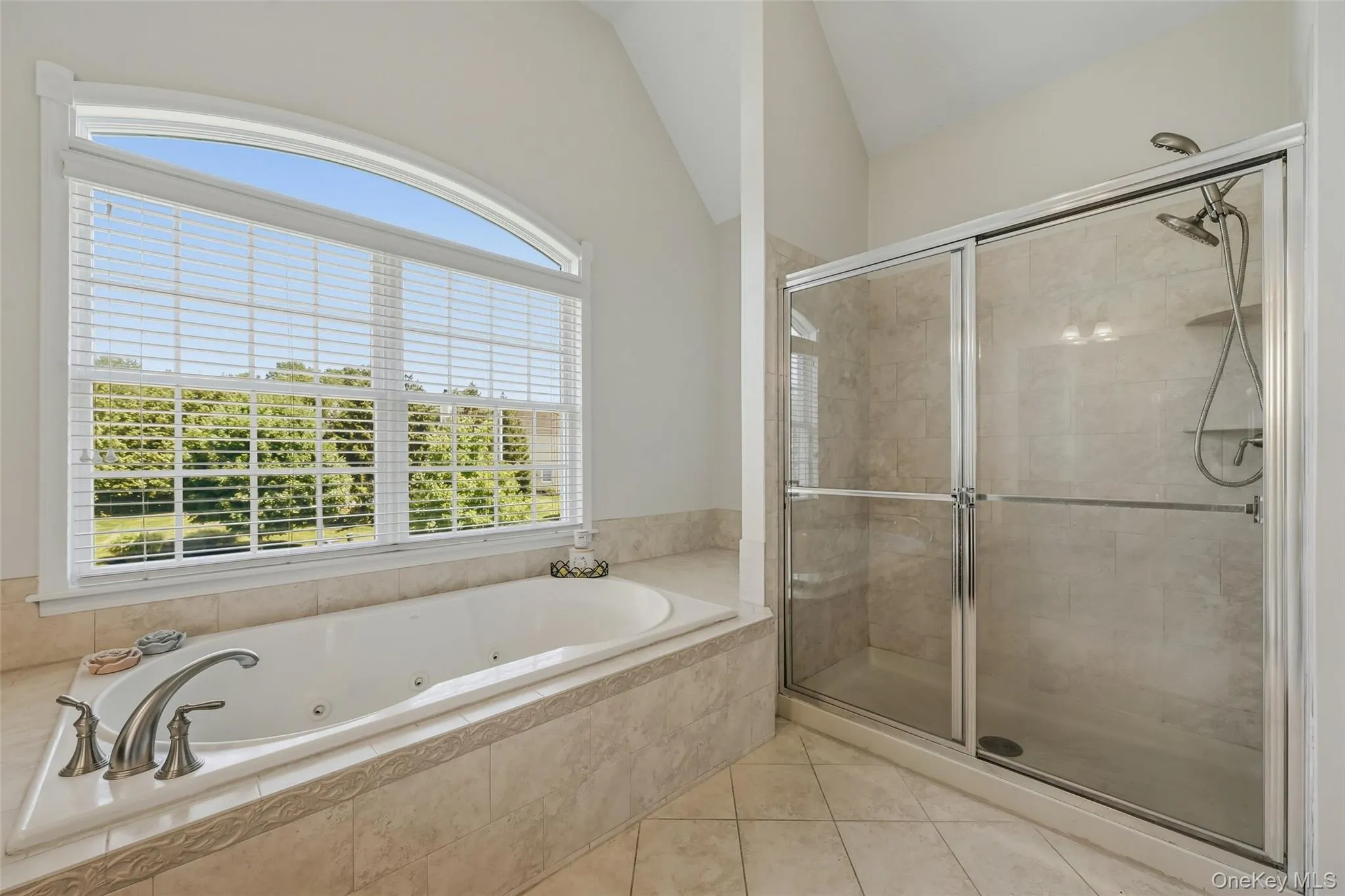 Soaking tub with jetted features, a large arched window, a tiled shower enclosure with sliding glass doors, a dual shower head system, and tiled flooring Soaking tub with jetted features, a large arched window, a tiled shower enclosure with sliding glass doors, a dual shower head system, and tiled flooring