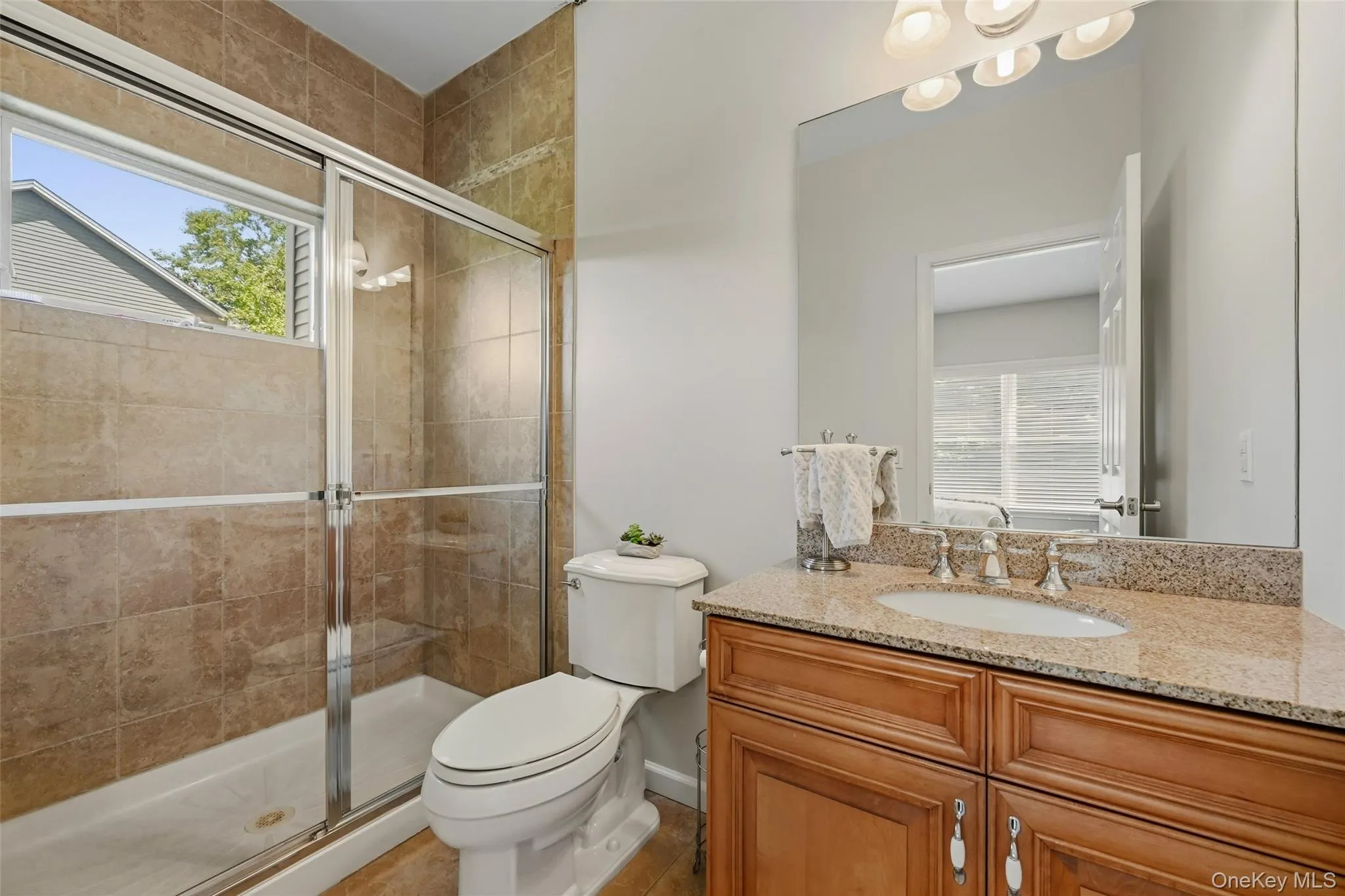 Bathroom featuring a glass-enclosed shower with tile surround, a vanity with wood cabinetry, and a stone countertop with an undermount sink Bathroom featuring a glass-enclosed shower with tile surround, a vanity with wood cabinetry, and a stone countertop with an undermount sink