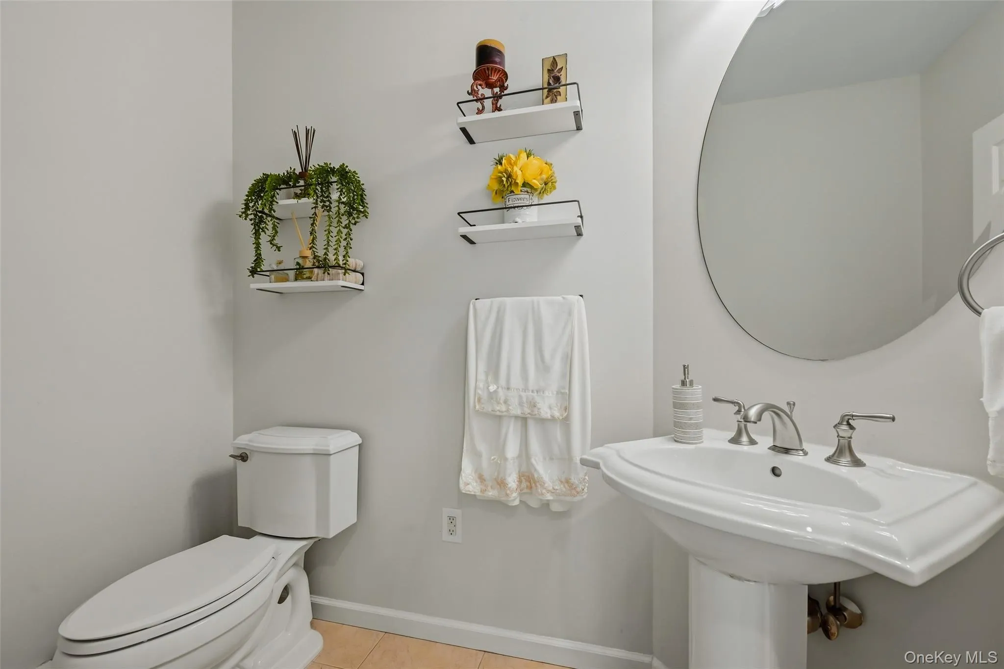 Pedestal sink with brushed nickel faucet, round wall-mounted mirror, and light wood-finish flooring Pedestal sink with brushed nickel faucet, round wall-mounted mirror, and light wood-finish flooring