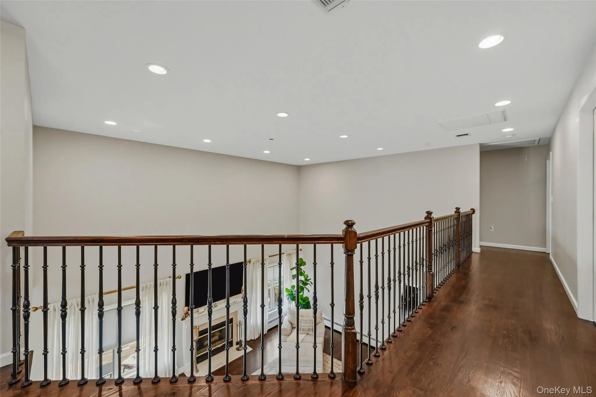 Hardwood flooring throughout the upper level landing, featuring a wrought iron and wood banister overlooking the space below Hardwood flooring throughout the upper level landing, featuring a wrought iron and wood banister overlooking the space below