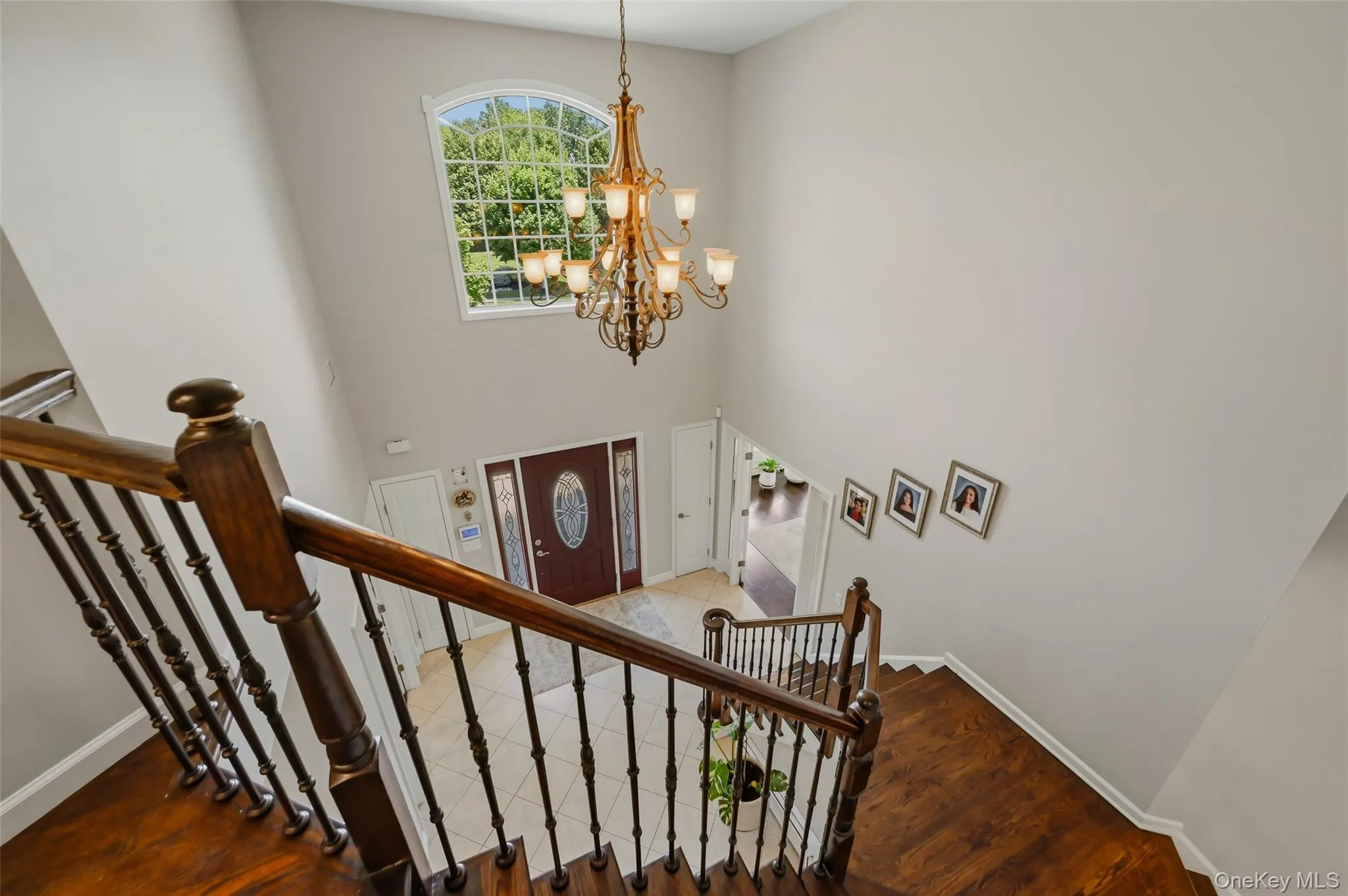 Two-story foyer featuring an arched transom window, a multi-tier chandelier, and a wood-finish staircase with wrought iron balusters Two-story foyer featuring an arched transom window, a multi-tier chandelier, and a wood-finish staircase with wrought iron balusters