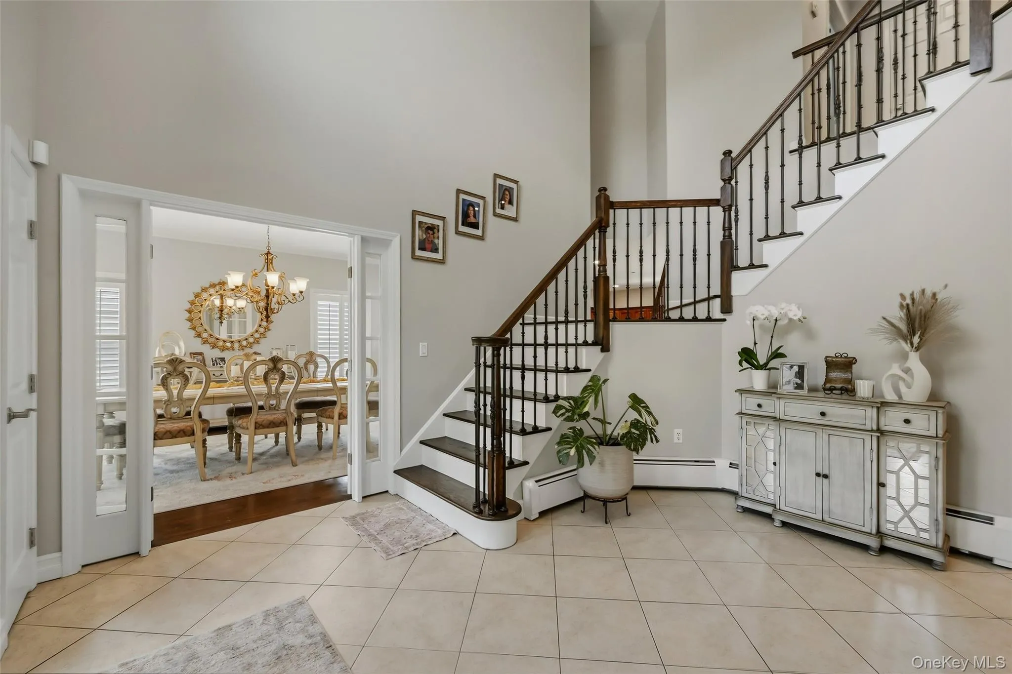 Spacious foyer featuring light-toned tile flooring, a dark wood-finish staircase with black balusters, and a double-height ceiling Spacious foyer featuring light-toned tile flooring, a dark wood-finish staircase with black balusters, and a double-height ceiling