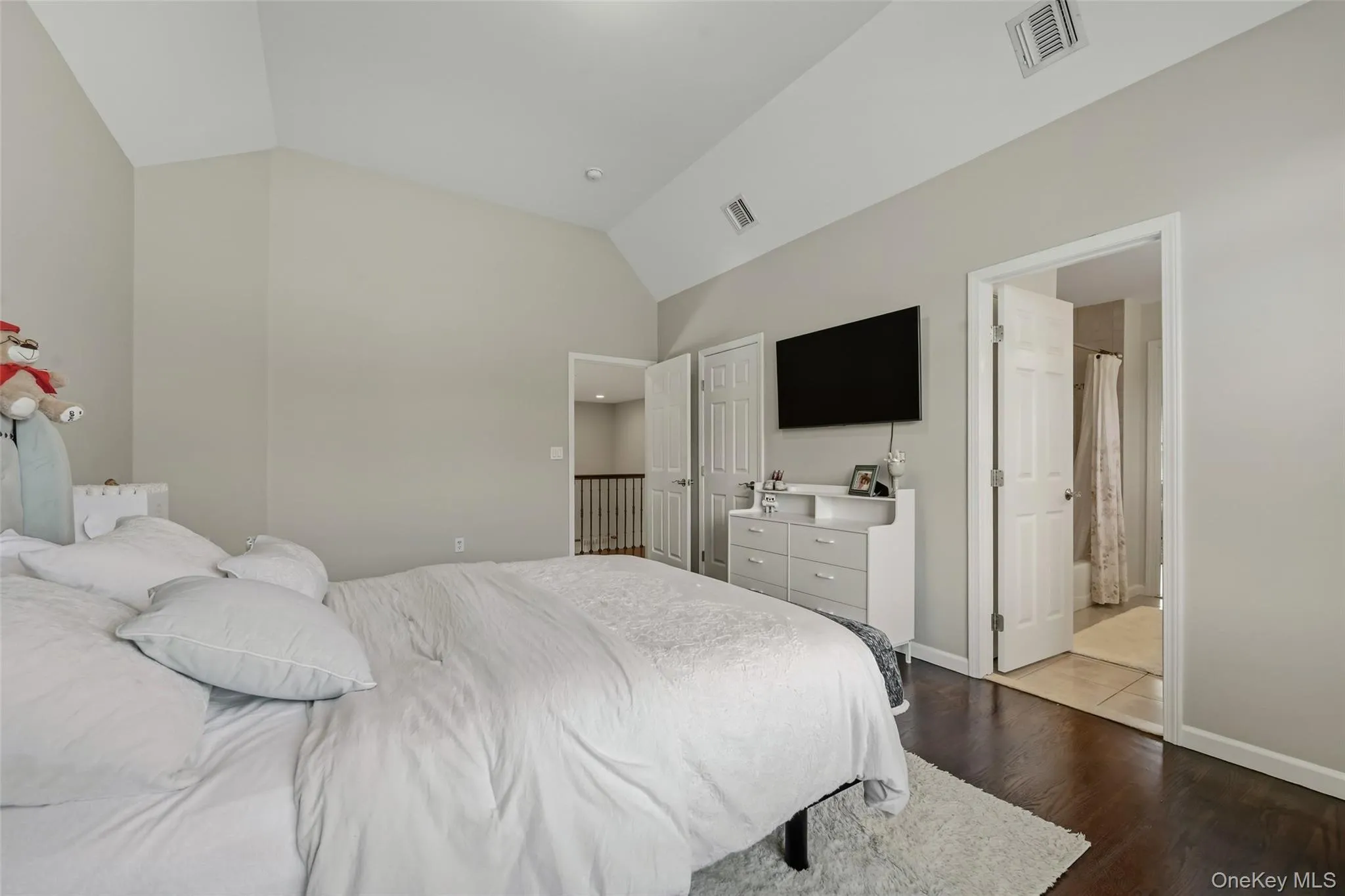 Vaulted ceiling bedroom with dark wood-finish flooring, light wall paint, and a white six-panel door Vaulted ceiling bedroom with dark wood-finish flooring, light wall paint, and a white six-panel door