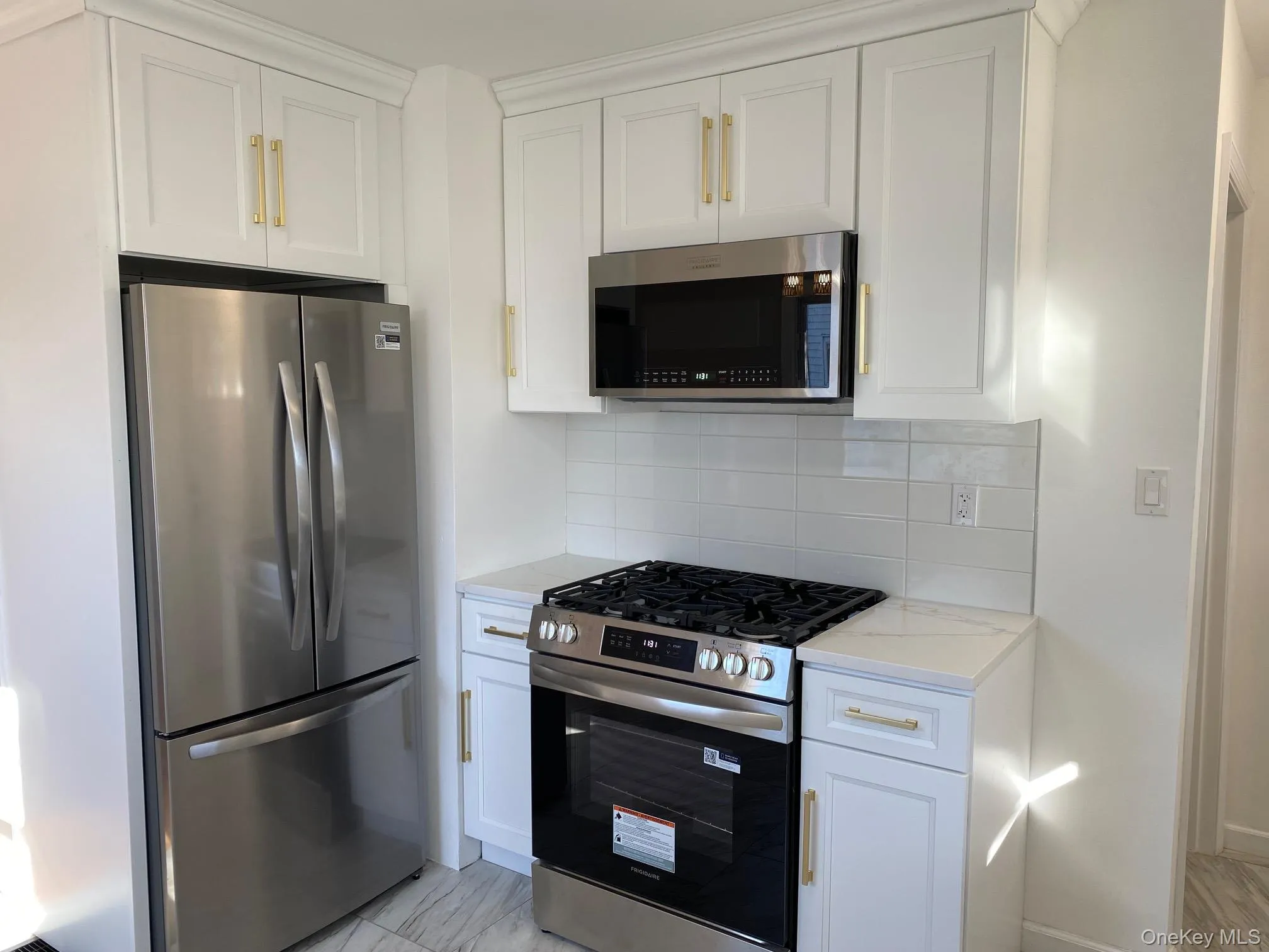 Kitchen with stainless steel appliances, tasteful backsplash, white cabinetry, and light stone counters Kitchen with stainless steel appliances, tasteful backsplash, white cabinetry, and light stone counters