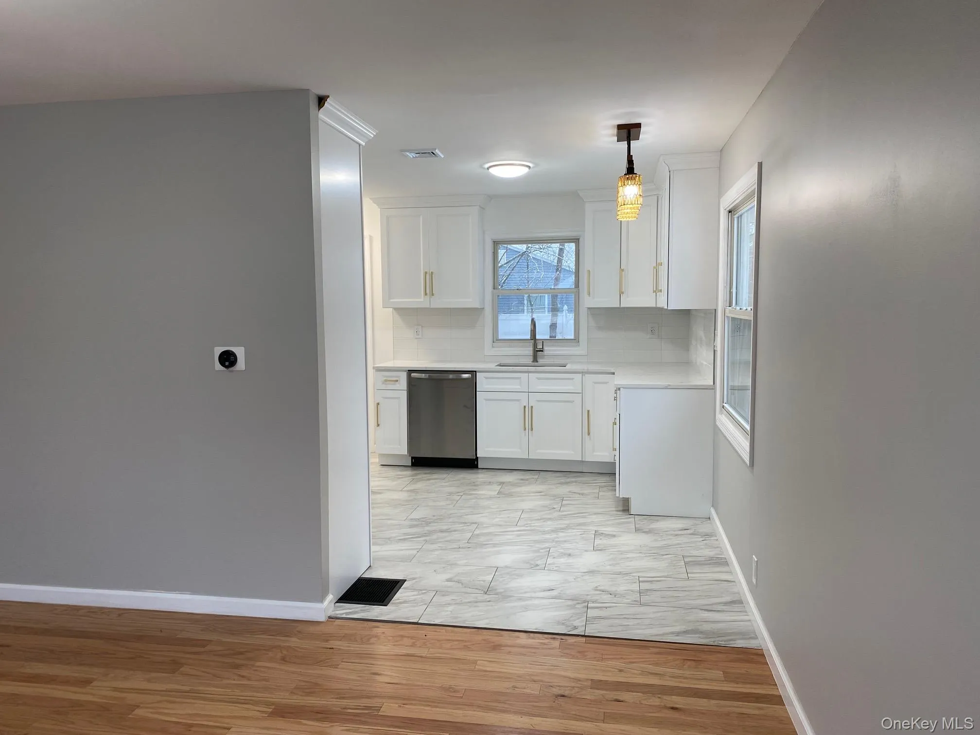 Kitchen featuring white cabinets, light wood-type flooring, dishwasher, hanging light fixtures, and backsplash Kitchen featuring white cabinets, light wood-type flooring, dishwasher, hanging light fixtures, and backsplash