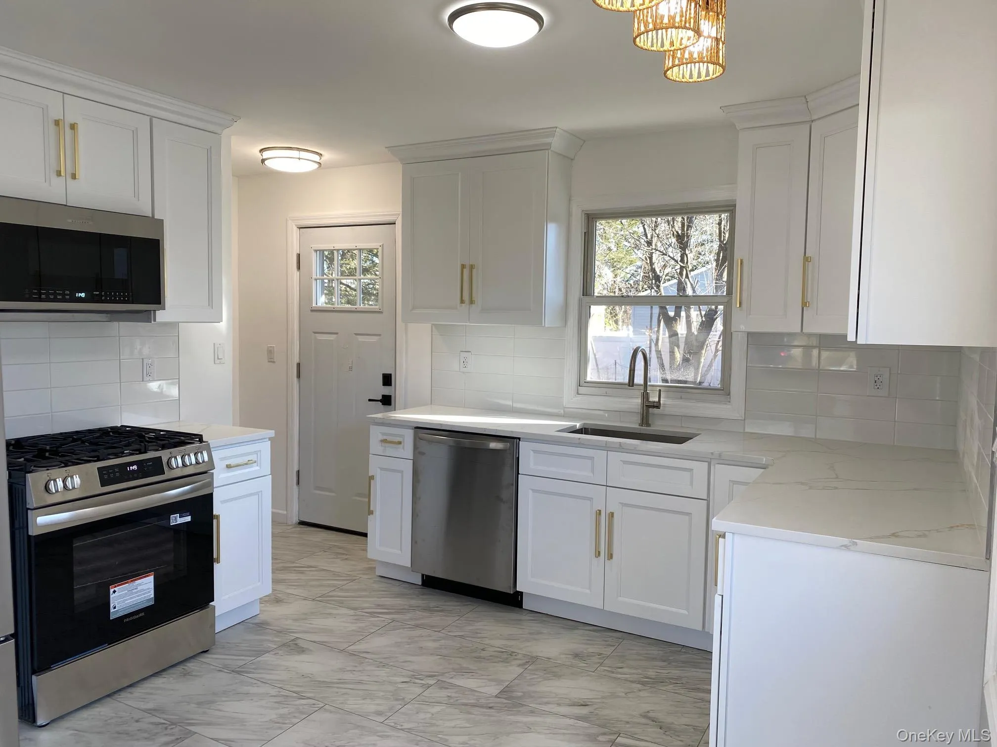 Kitchen with appliances with stainless steel finishes, tasteful backsplash, white cabinets, and light marble finish floors Kitchen with appliances with stainless steel finishes, tasteful backsplash, white cabinets, and light marble finish floors