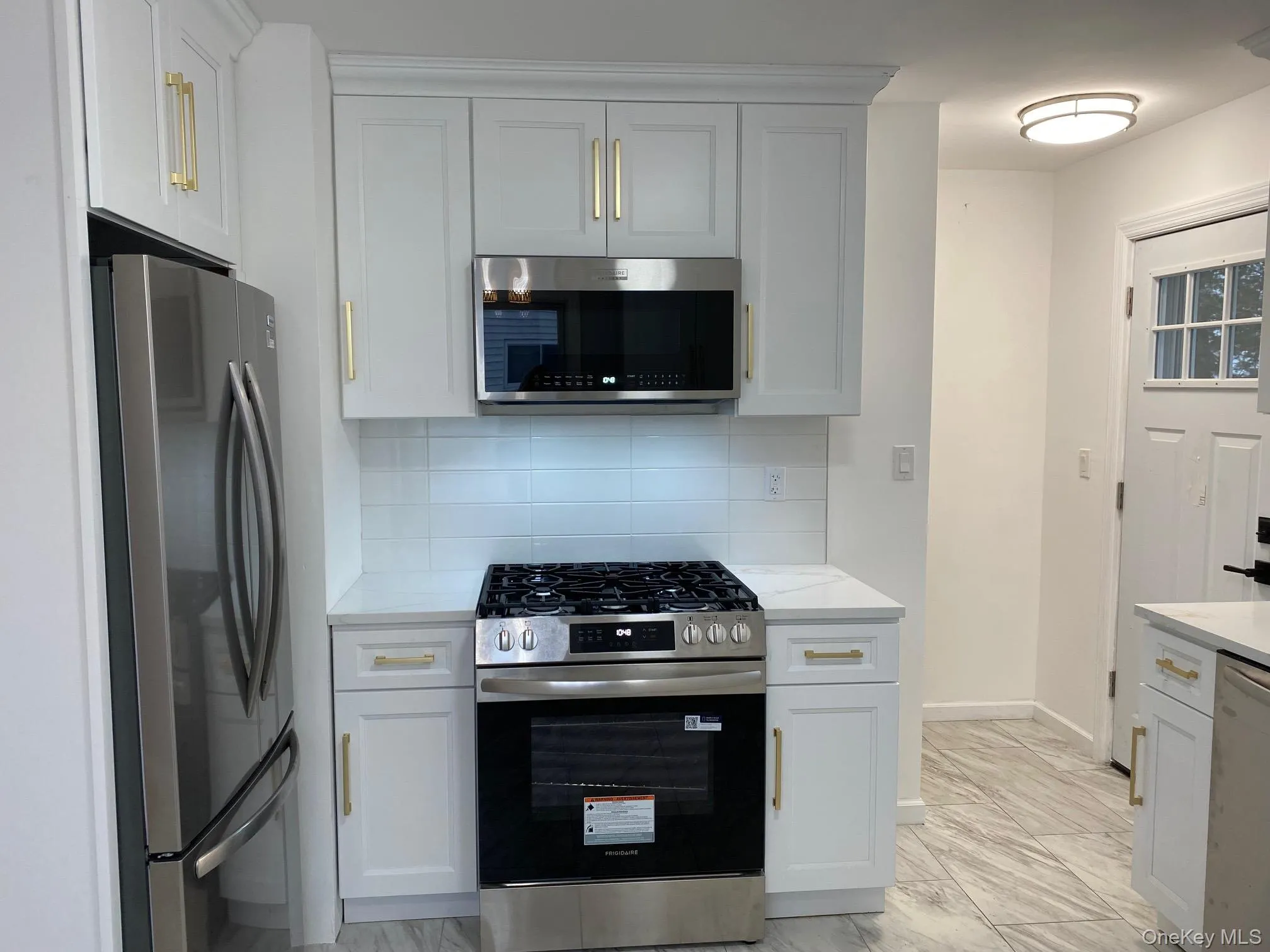 Kitchen with appliances with stainless steel finishes, backsplash, light marble finish floors, and white cabinets Kitchen with appliances with stainless steel finishes, backsplash, light marble finish floors, and white cabinets